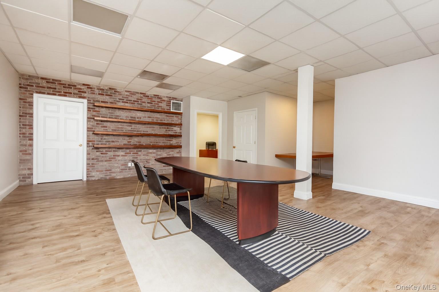 (Digitally Decluttered) Home office featuring brick wall, light wood-style flooring, and a paneled ceiling