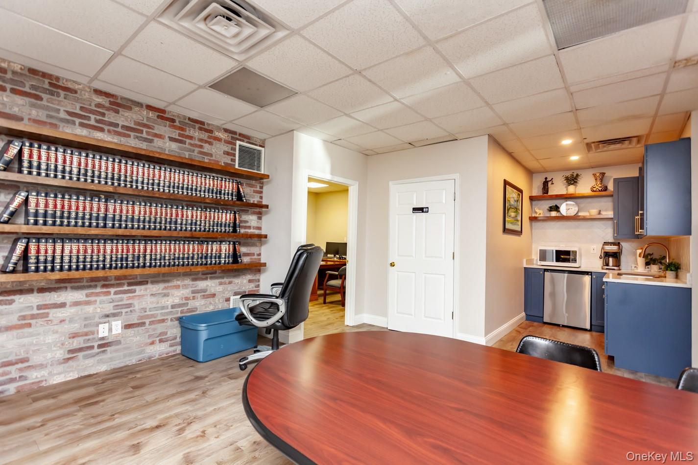 Office area with brick wall, light wood-style flooring, and a paneled ceiling