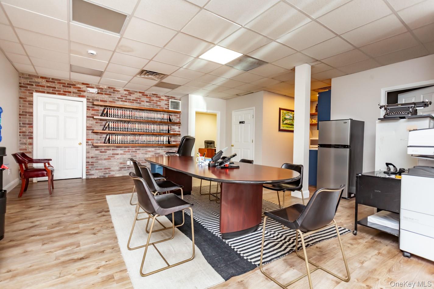 Home office with brick wall, light wood-style flooring, and a drop ceiling