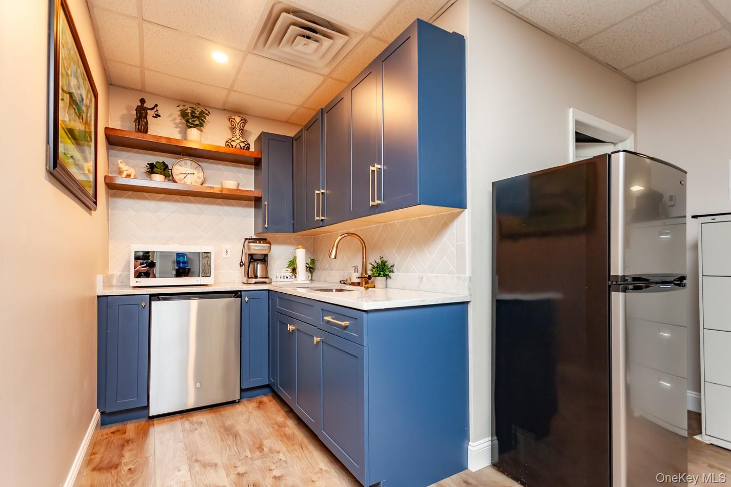 Kitchen with a paneled ceiling, freestanding refrigerator, tasteful backsplash, open shelves, and stainless steel refrigerator