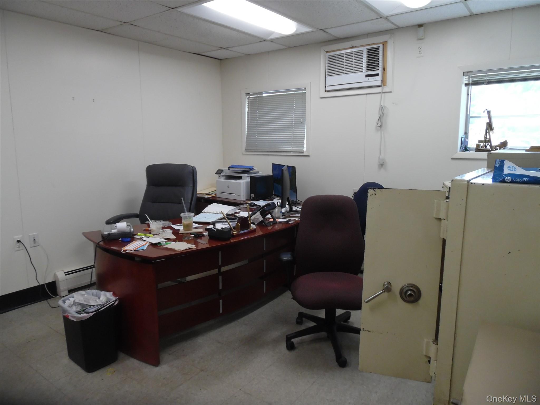 Office space featuring a paneled ceiling, a baseboard radiator, light floors, and a wall mounted air conditioner