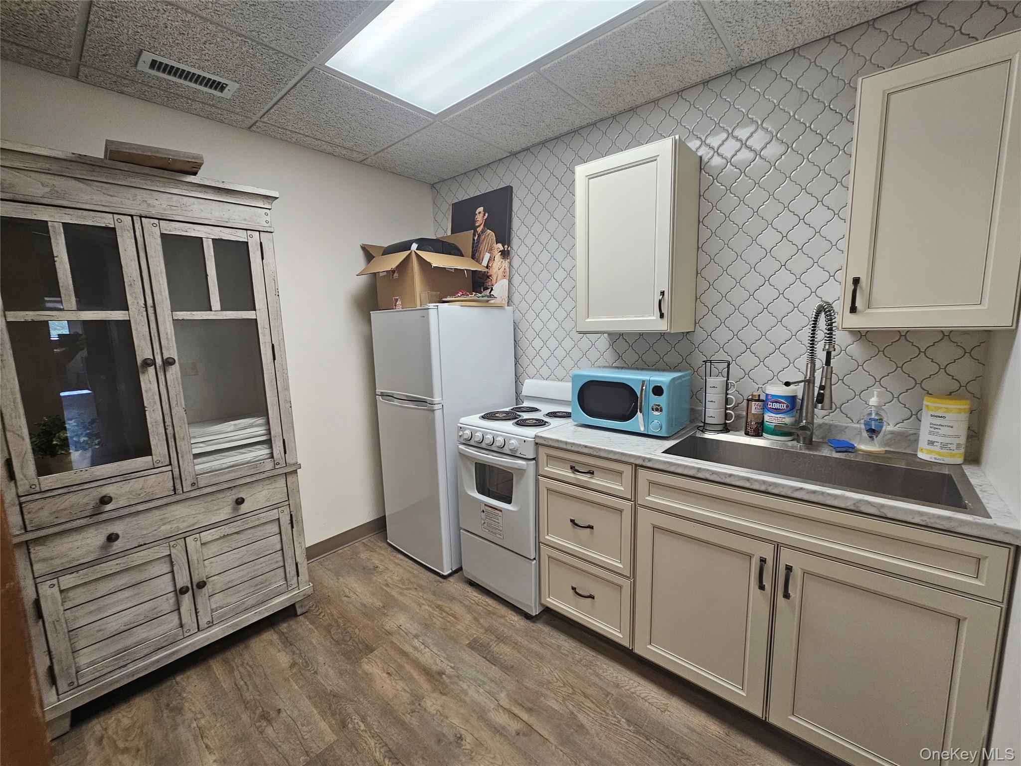 Kitchen with white appliances, light countertops, wood finished floors, decorative backsplash, and a drop ceiling