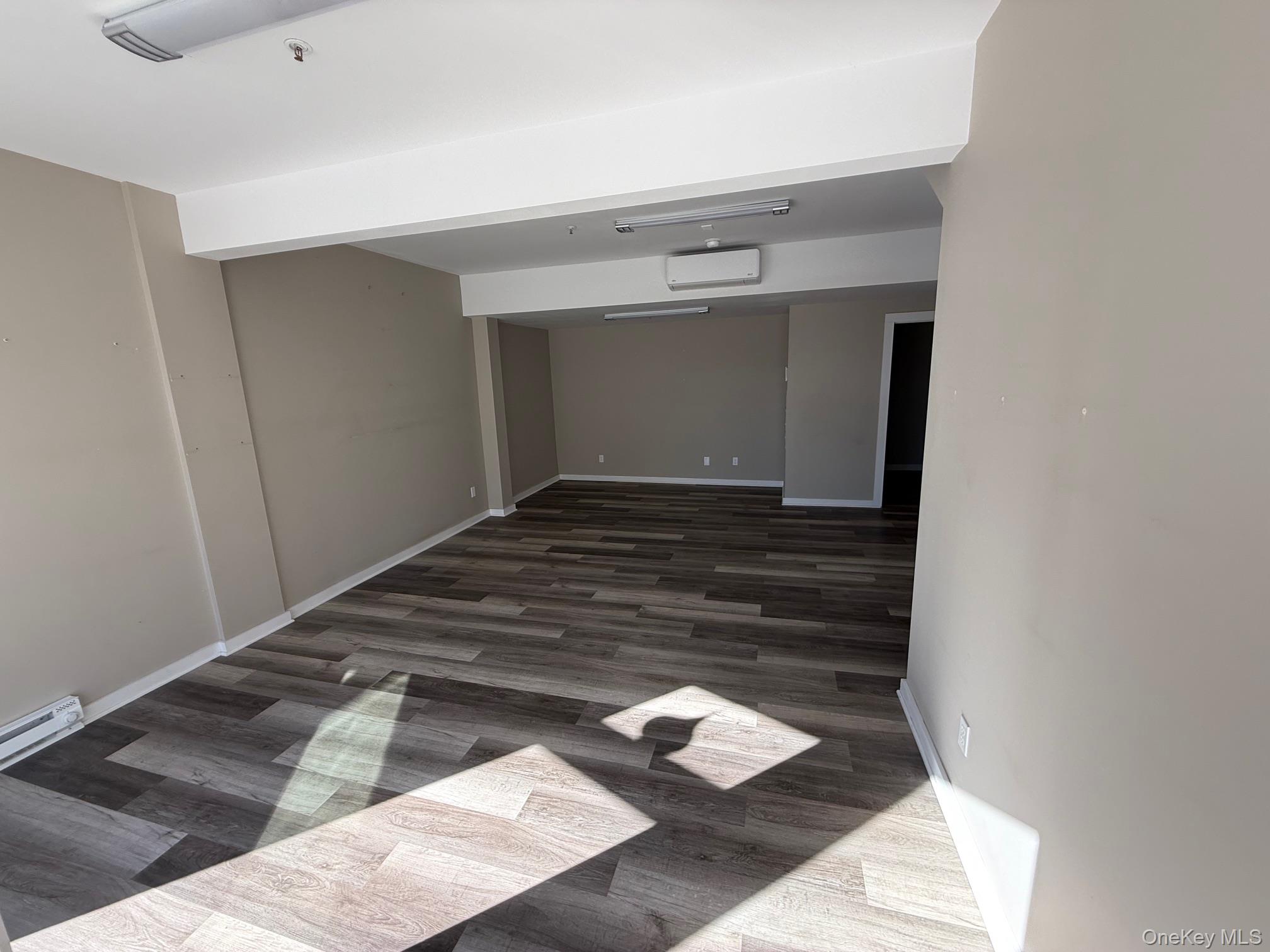 Spare room with dark wood-style floors and an AC wall unit