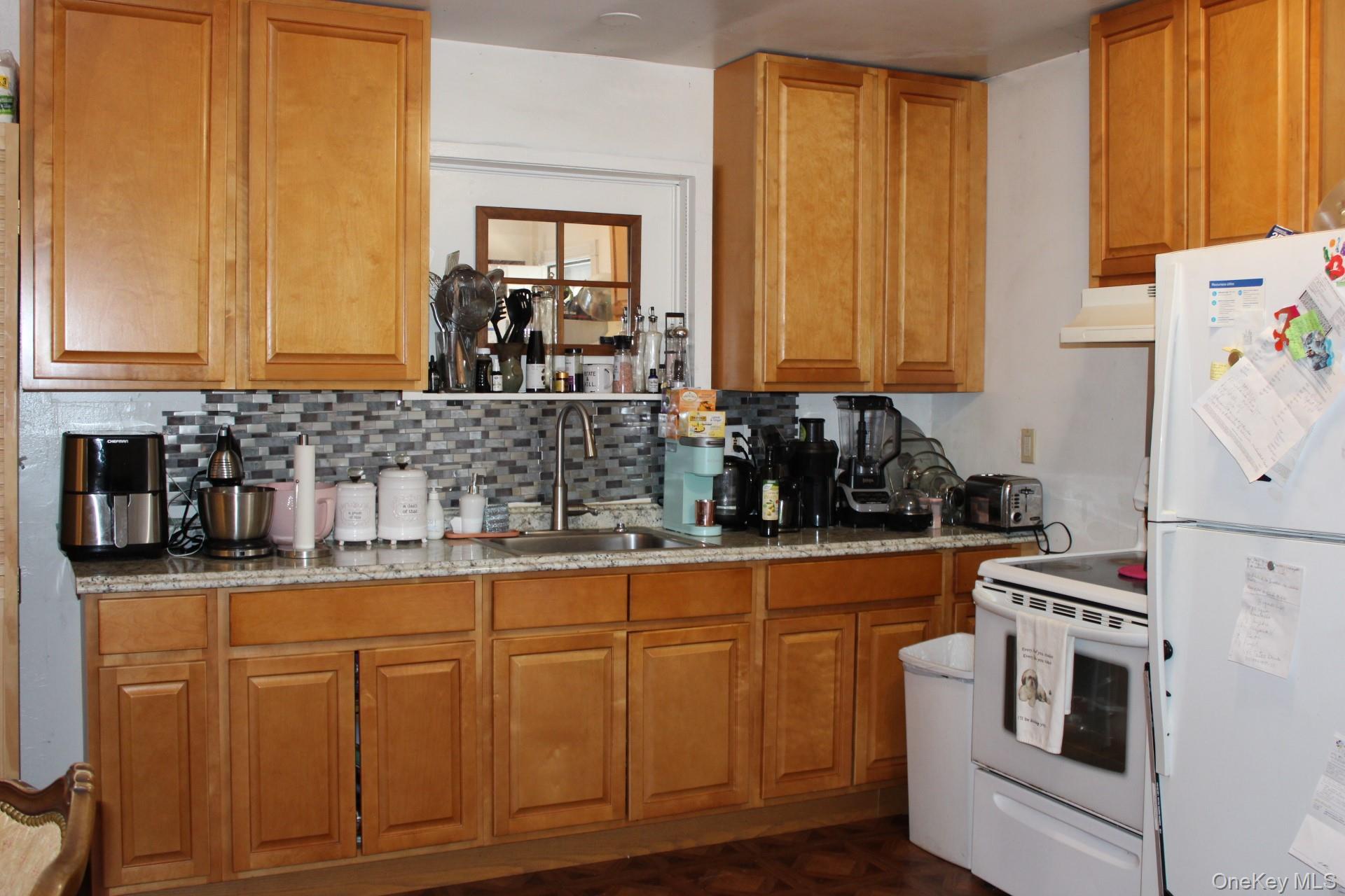 Kitchen with a sink, tasteful backsplash, brown cabinetry, under cabinet range hood, and white appliances