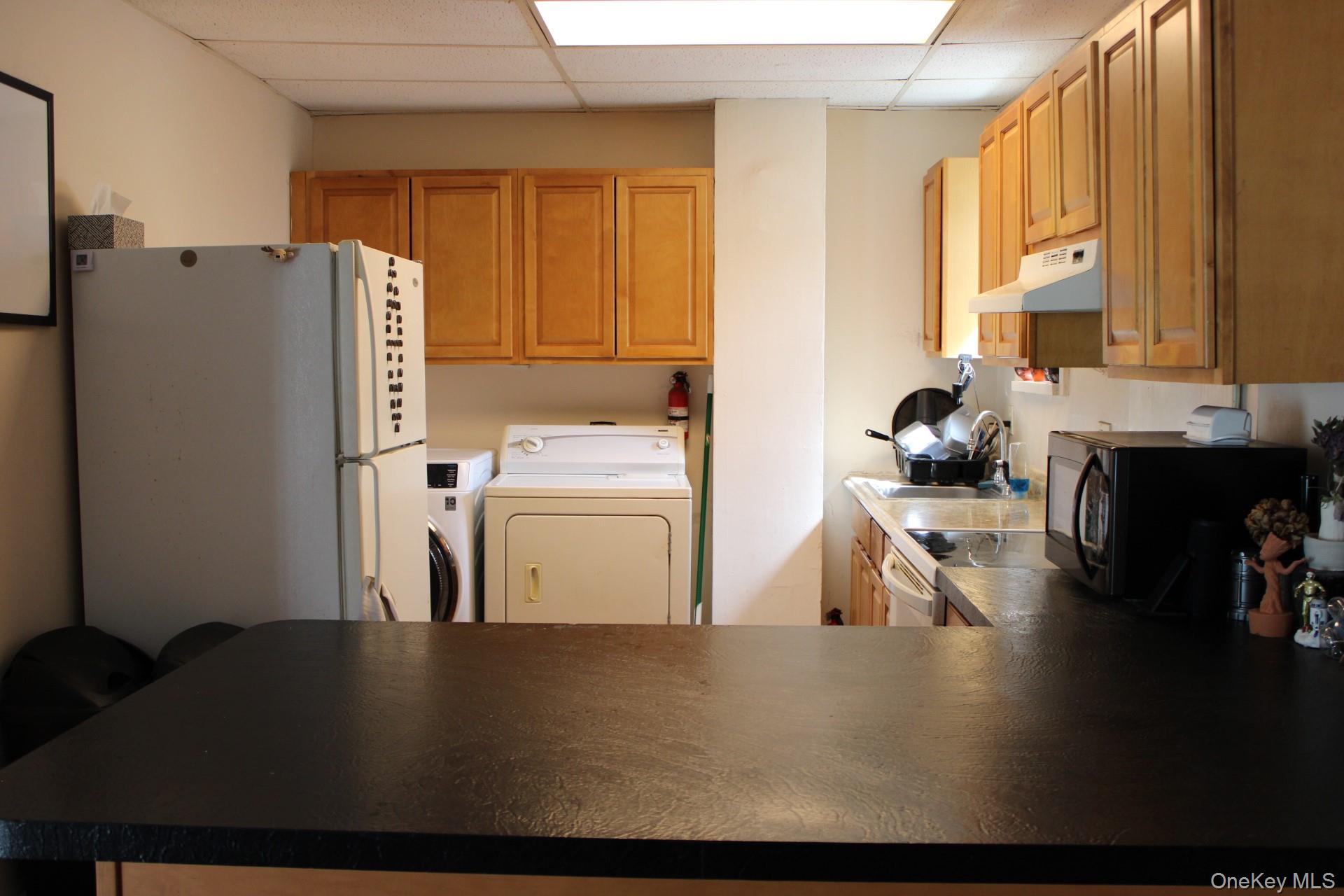 Kitchen with under cabinet range hood, a sink, black microwave, washer and clothes dryer, and freestanding refrigerator