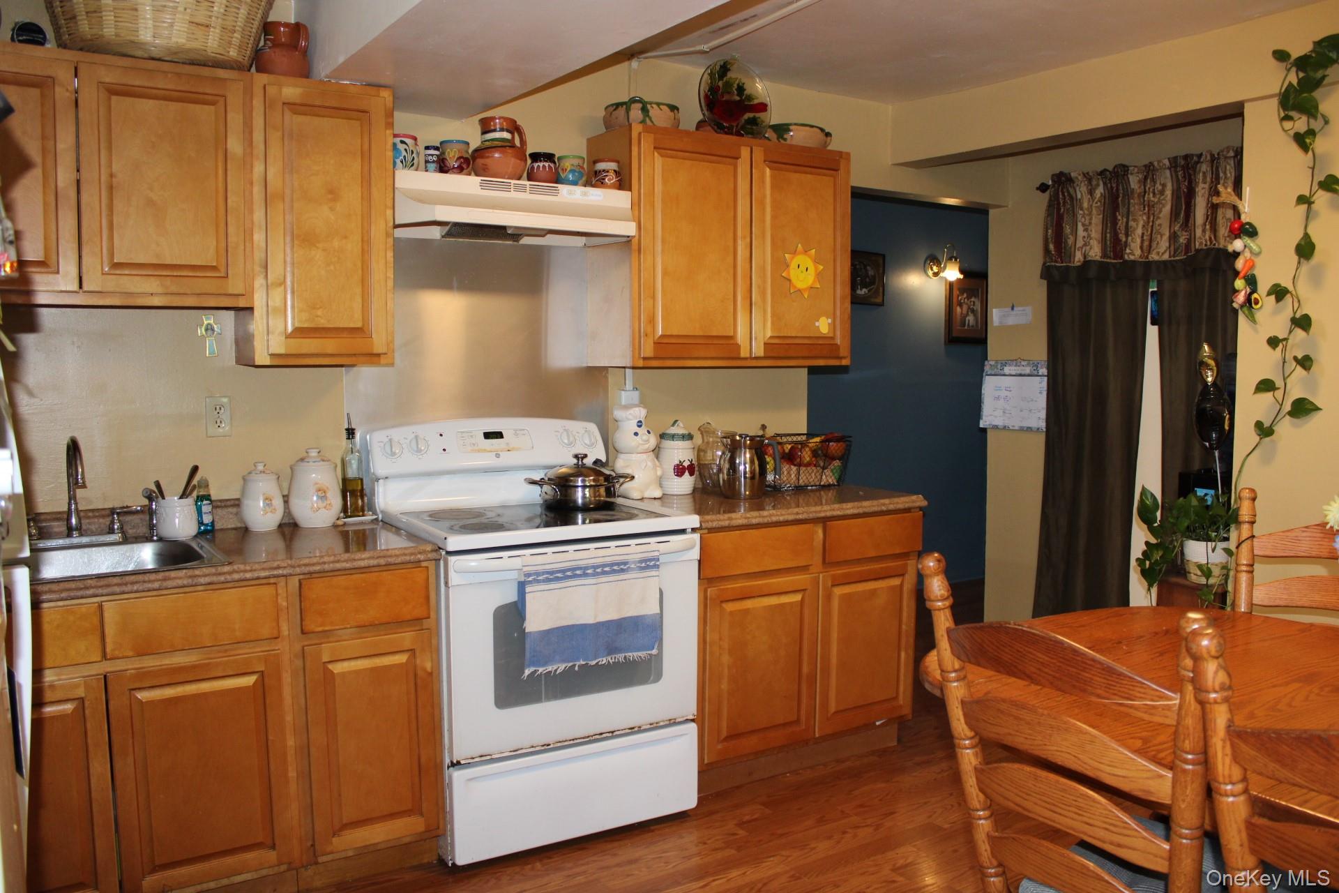 Kitchen featuring white electric range oven, under cabinet range hood, a sink, brown cabinetry, and wood finished floors