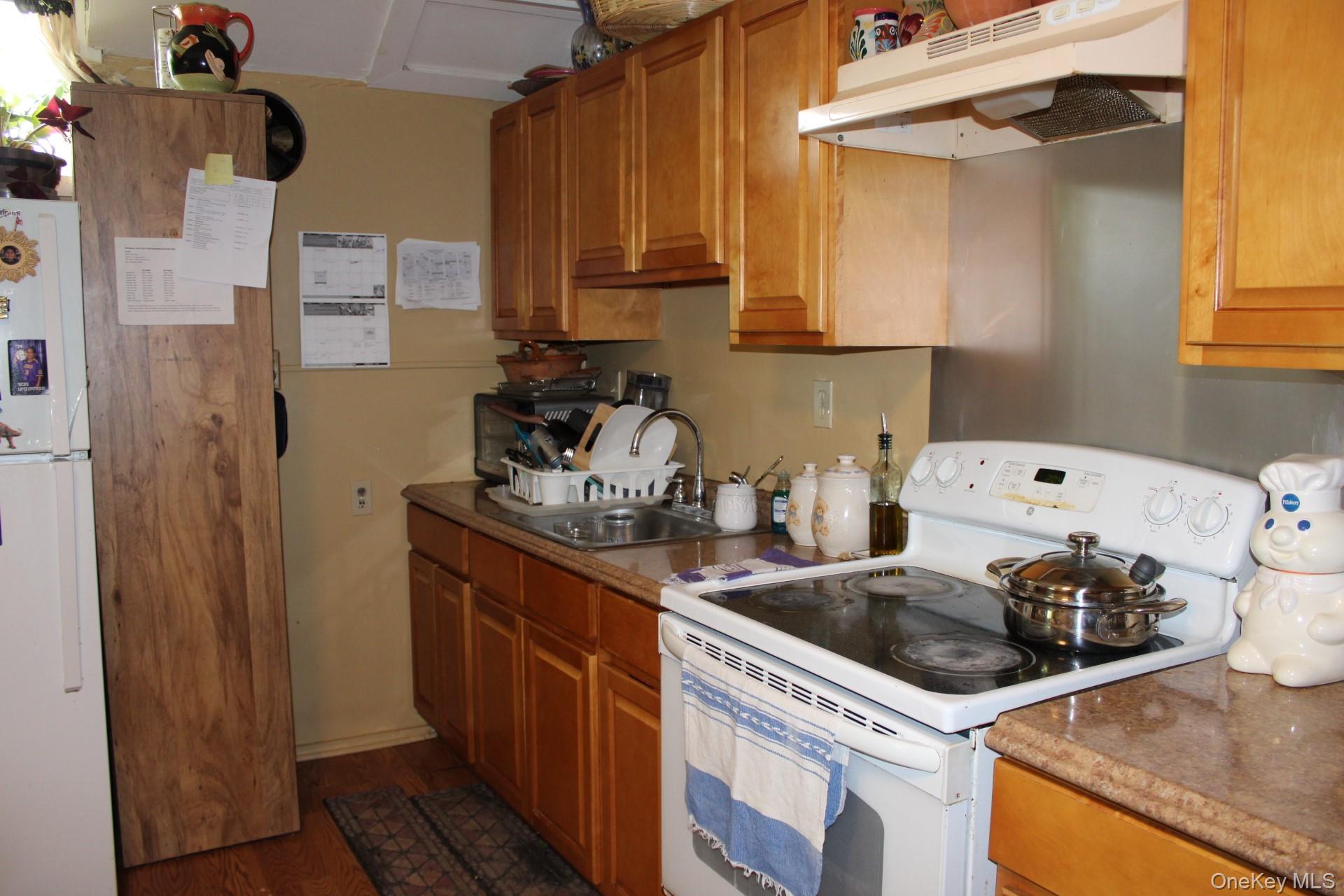 Kitchen featuring brown cabinets, a sink, under cabinet range hood, and white appliances