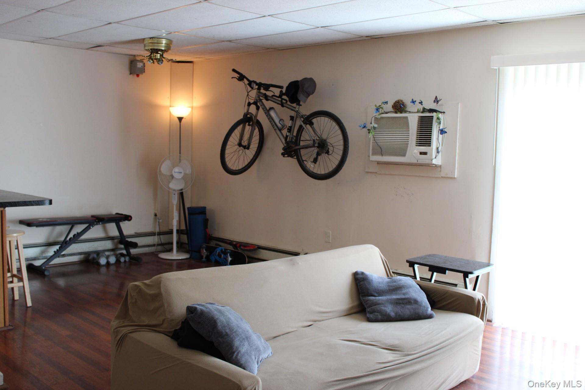 Living area with a drop ceiling, wood finished floors, an AC wall unit, and ceiling fan