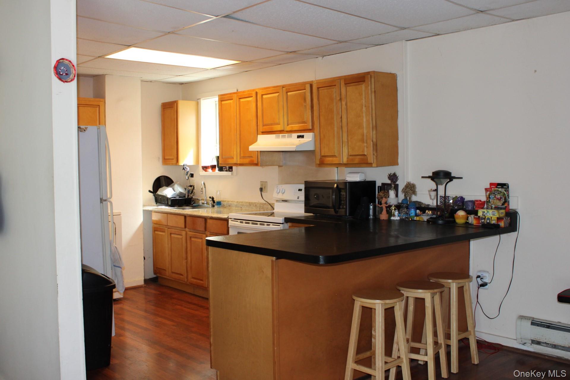 Kitchen featuring under cabinet range hood, a drop ceiling, a peninsula, and white appliances