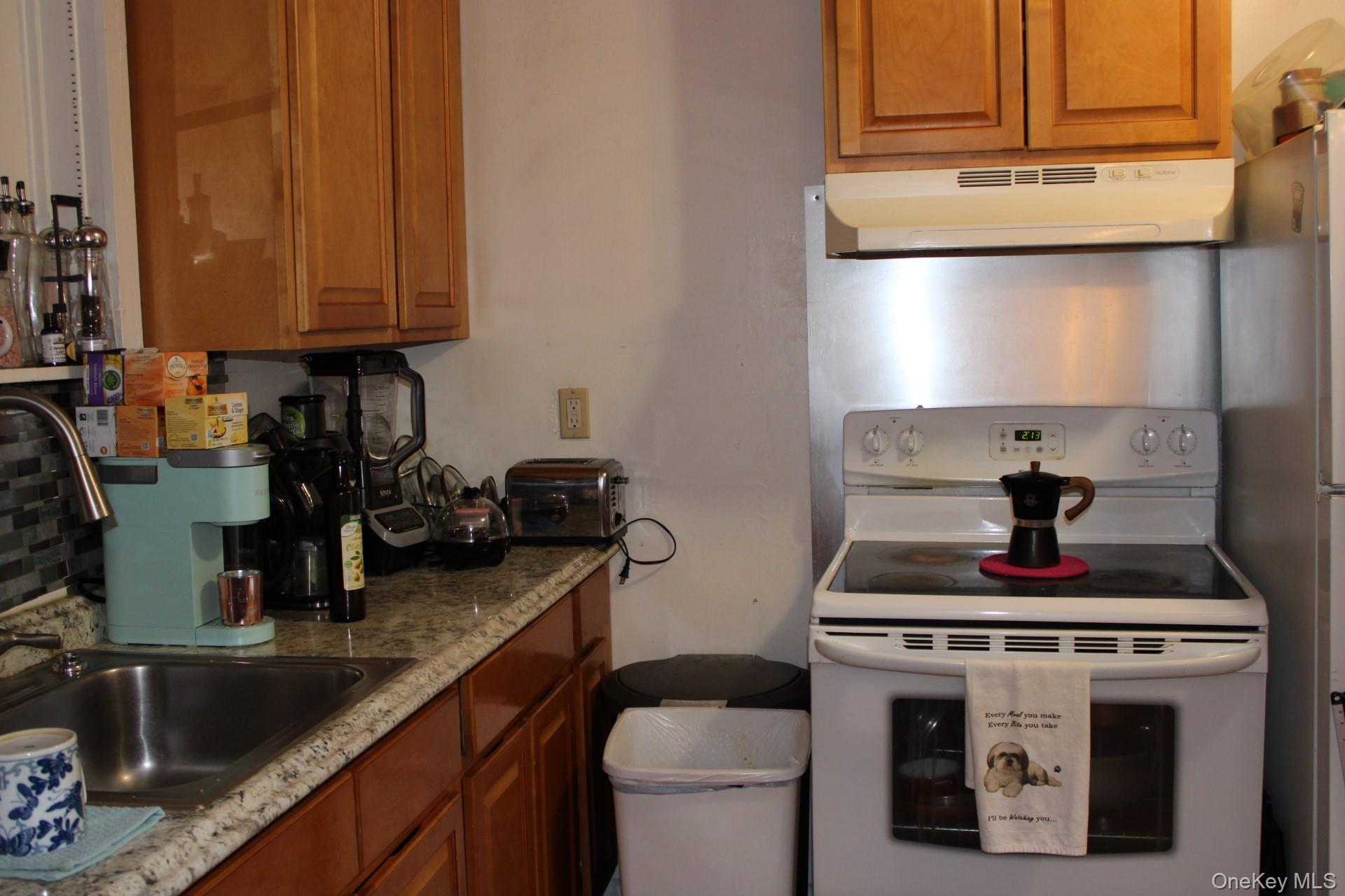 Kitchen with light stone counters, electric stove, brown cabinetry, and ventilation hood