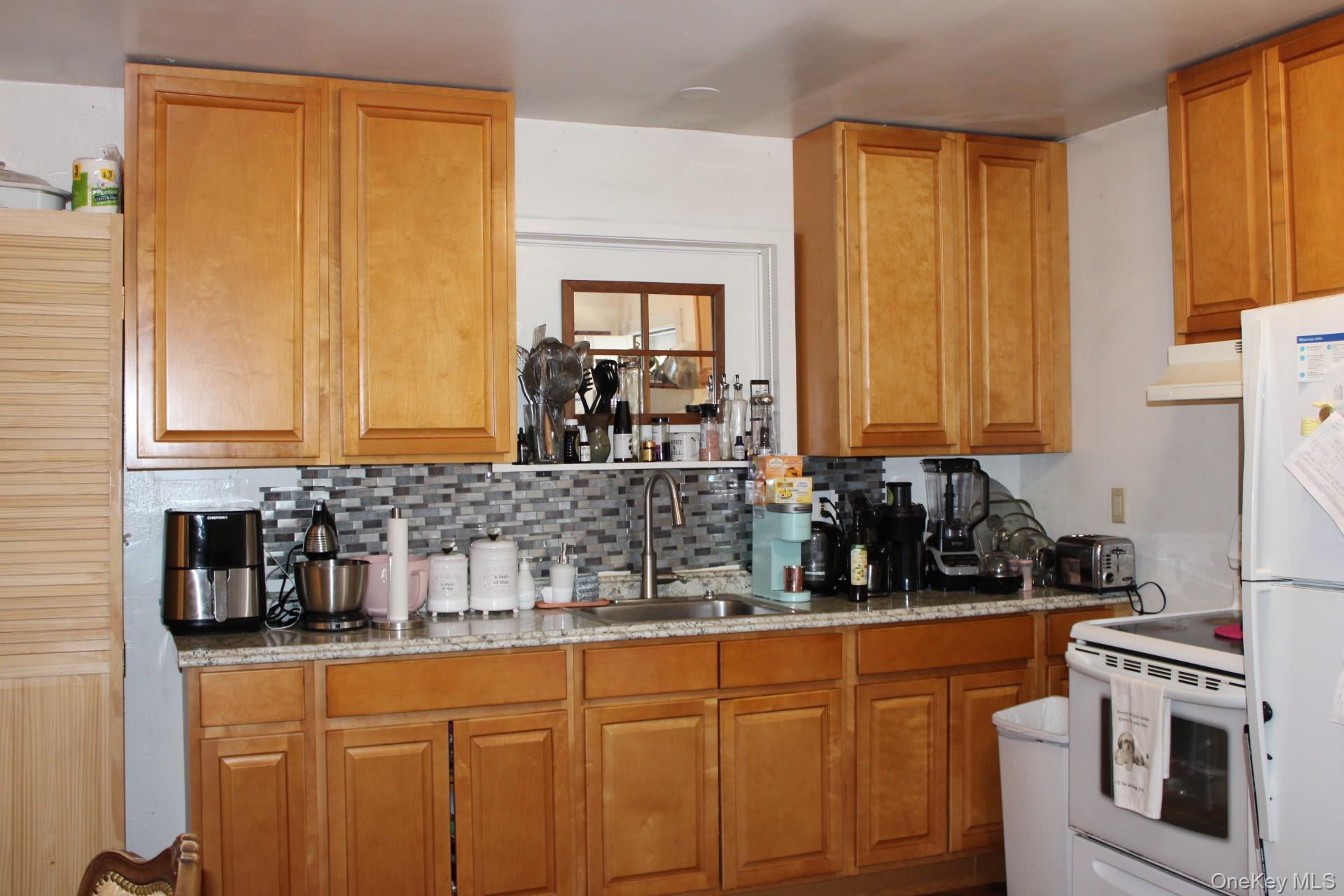 Kitchen with white appliances, under cabinet range hood, decorative backsplash, a sink, and brown cabinets