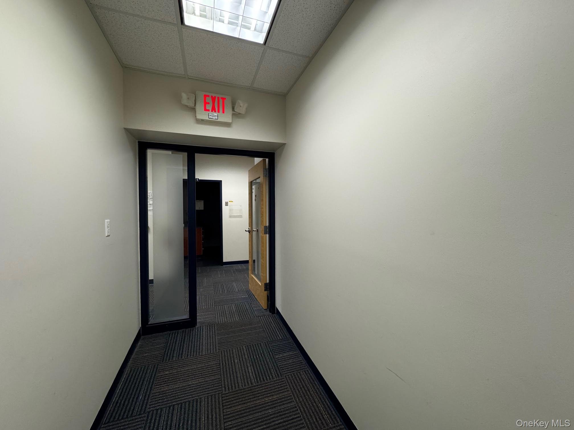 Hall featuring a drop ceiling and dark colored carpet