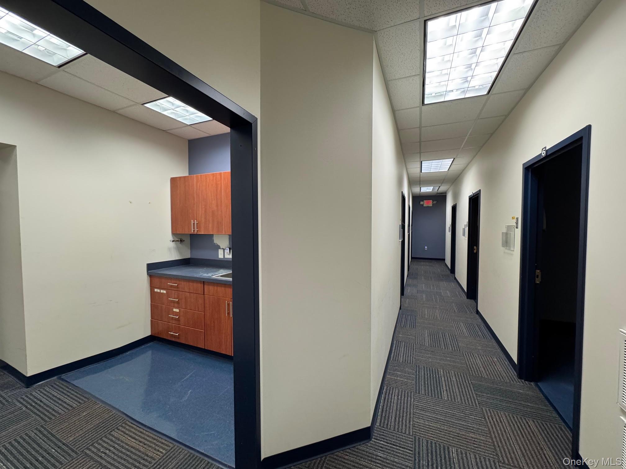 Hallway featuring a drop ceiling and dark colored carpet