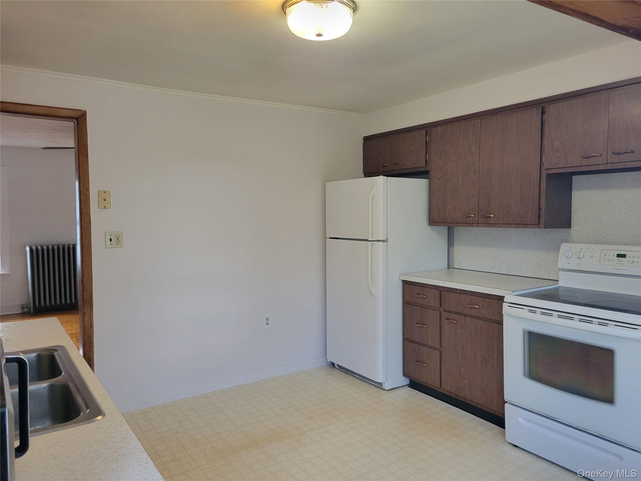 Kitchen featuring white appliances, light countertops, radiator, light floors, and dark brown cabinets