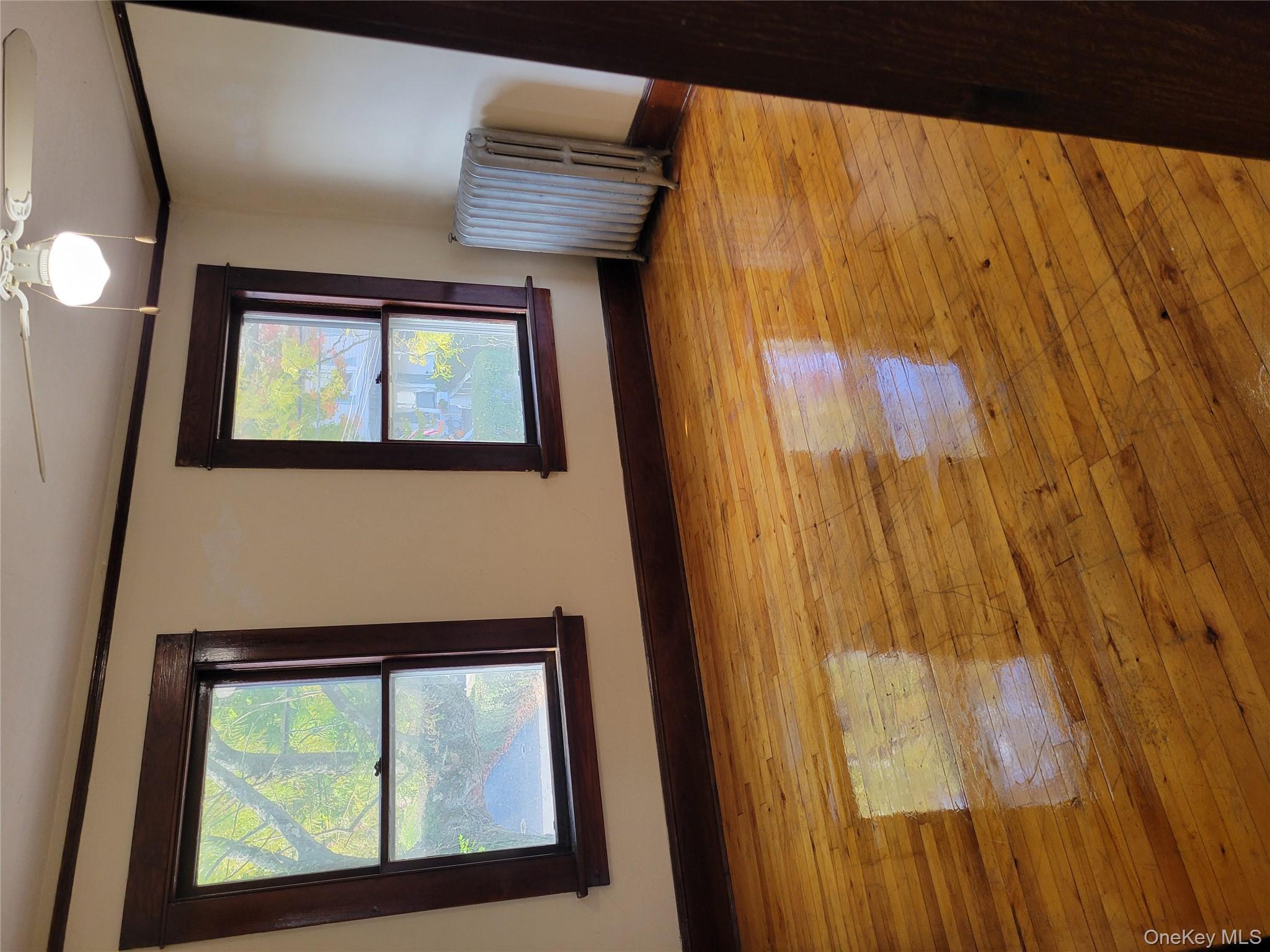 Empty room featuring light wood-style flooring, ornamental molding, and radiator heating unit