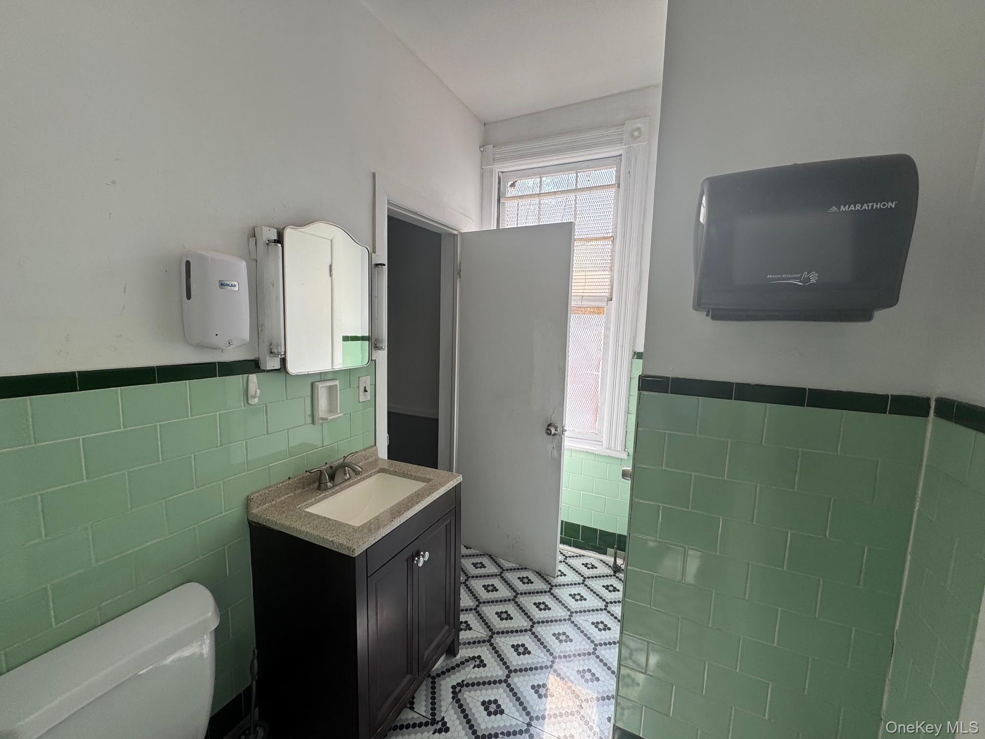 Half bath featuring tile walls, vanity, and wainscoting
