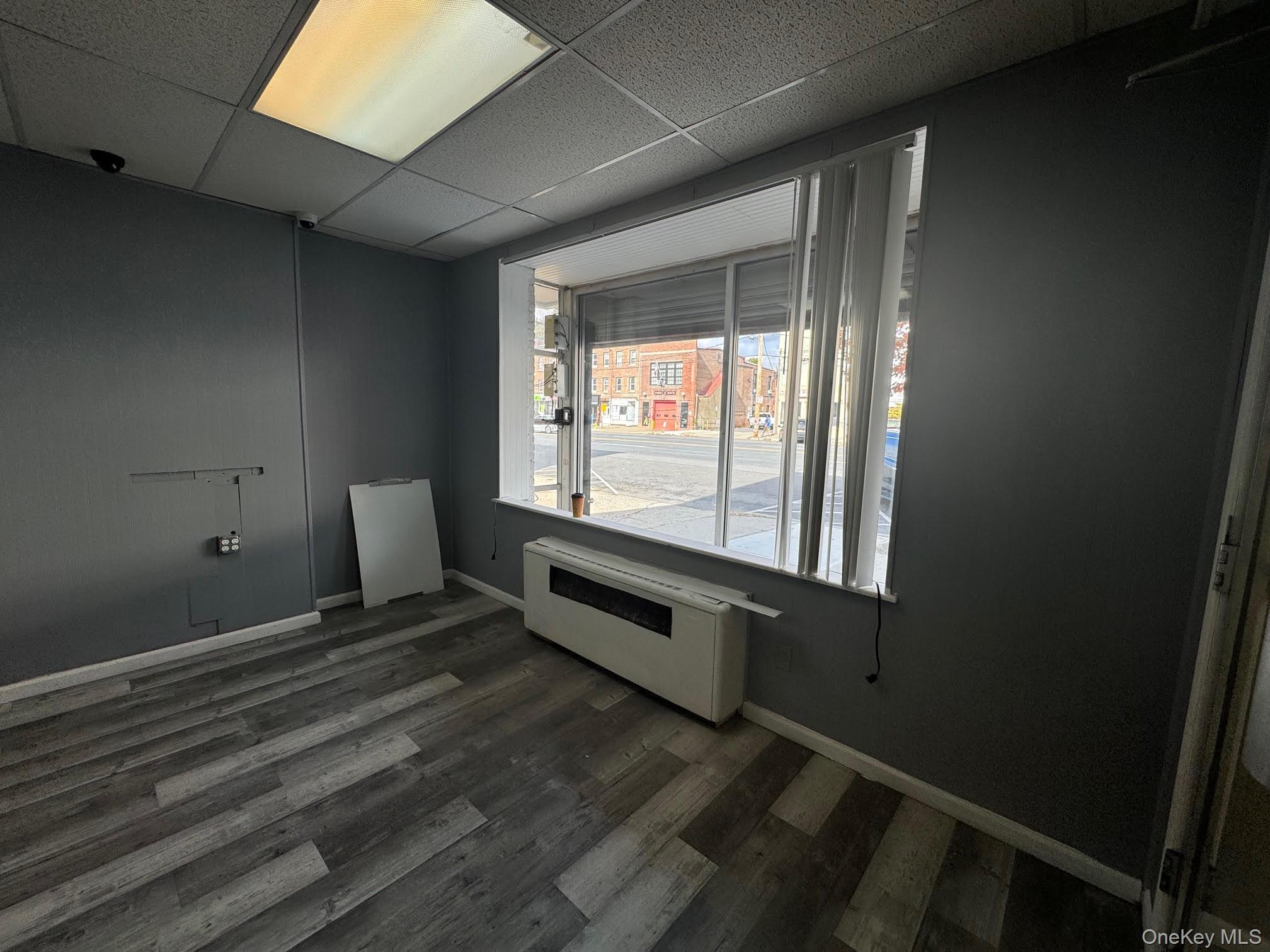 Unfurnished room featuring dark wood-style flooring, a paneled ceiling, and radiator