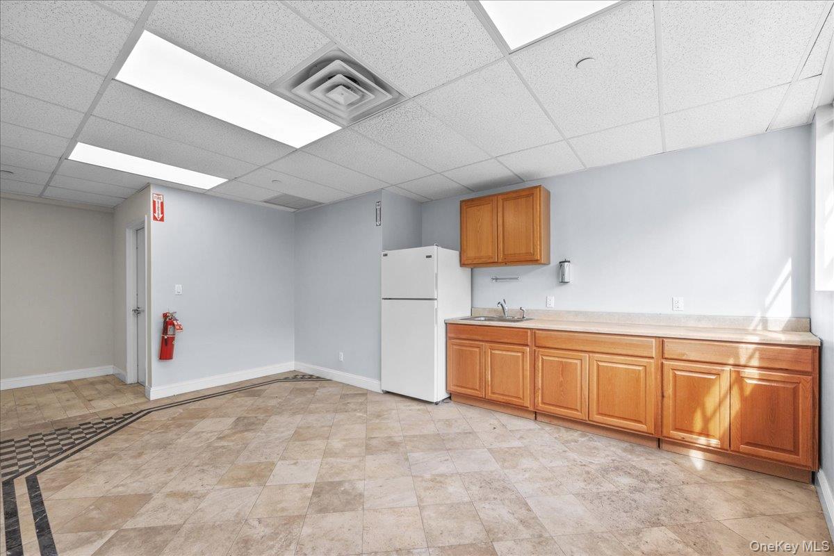 Kitchen featuring light countertops, freestanding refrigerator, a paneled ceiling, and brown cabinetry