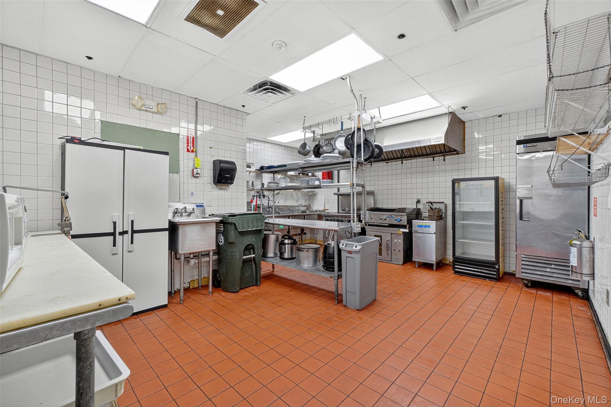Kitchen featuring tile walls, light countertops, white microwave, and stainless steel fridge