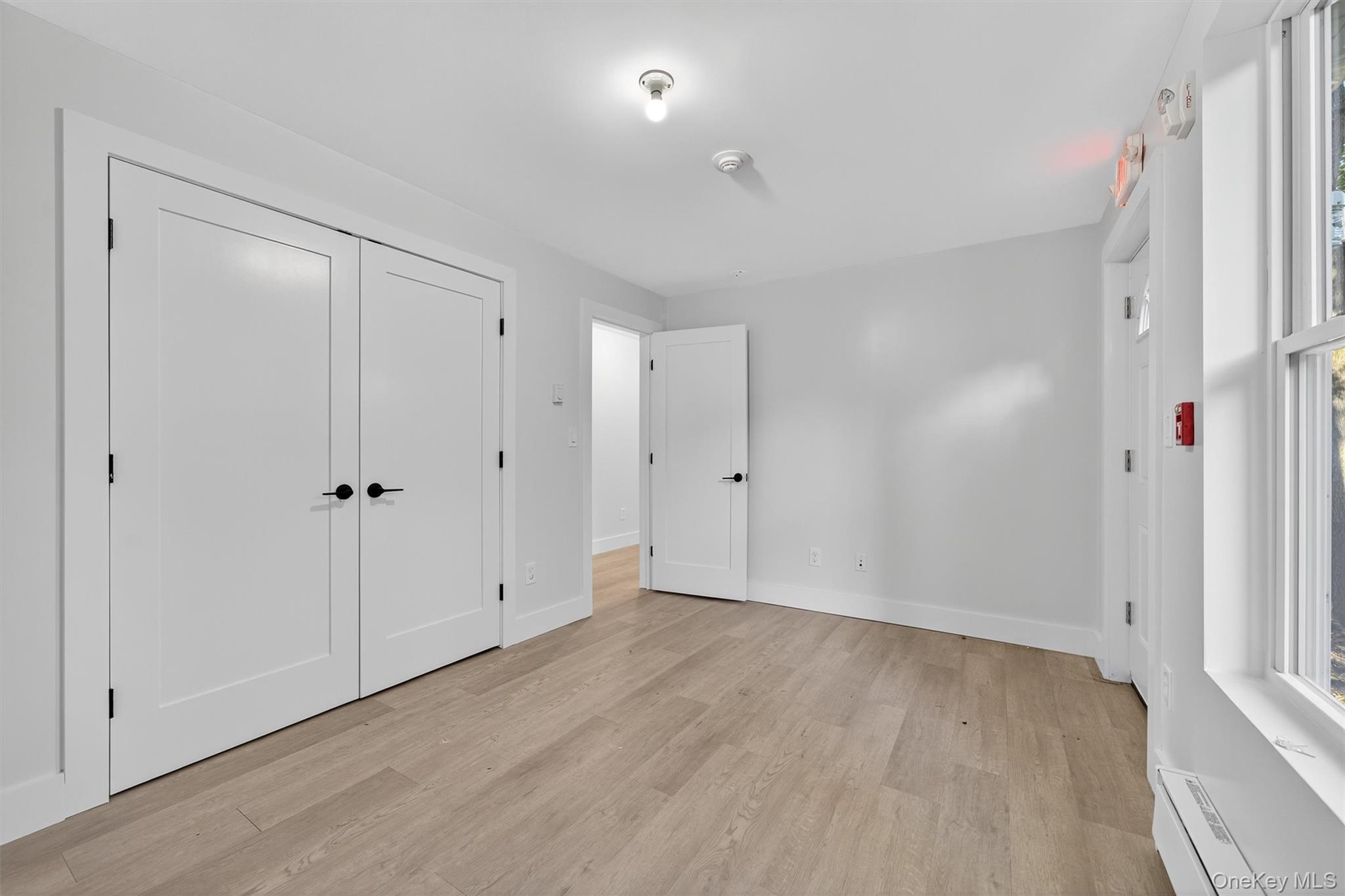 Unfurnished bedroom with a baseboard radiator, light wood-type flooring, and a closet
