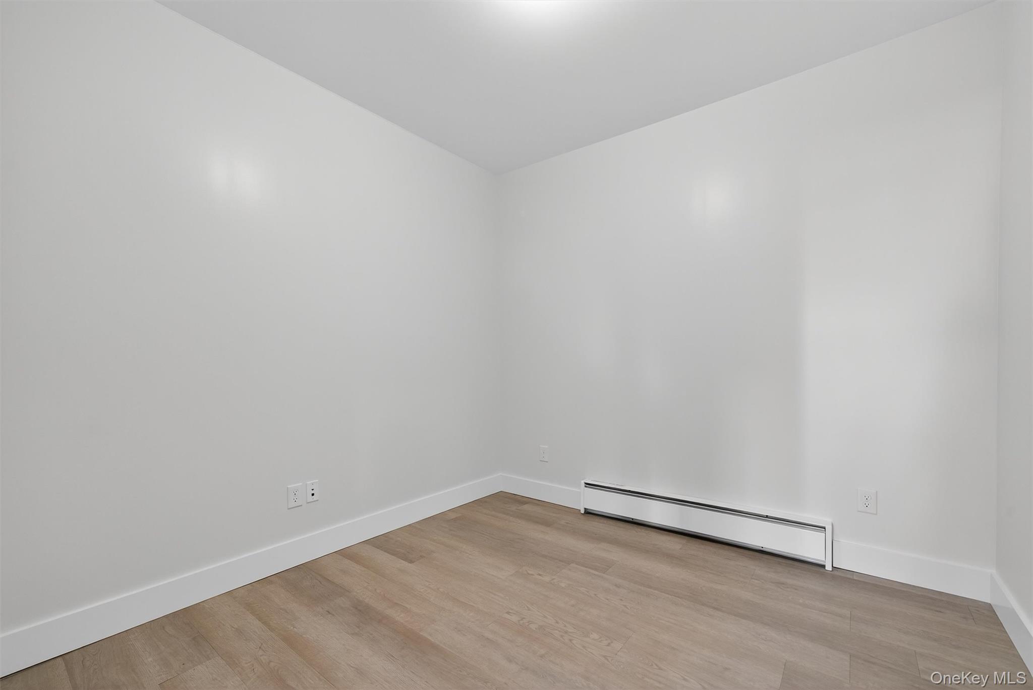 Spare room featuring a baseboard heating unit and light wood-type flooring