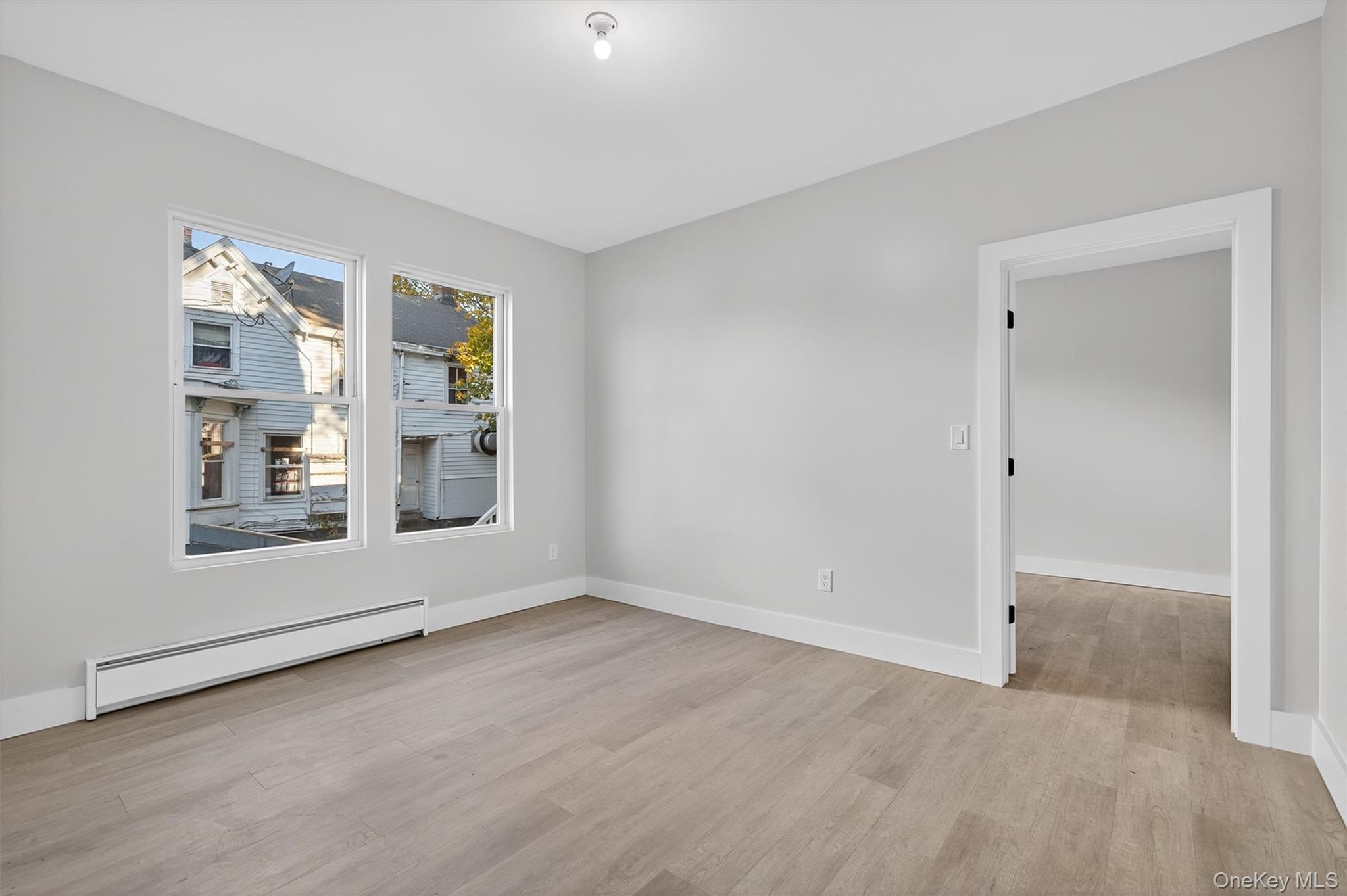 Empty room with baseboard heating and light wood-style floors