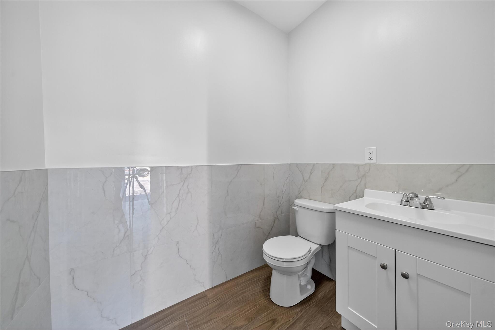 Half bathroom with tile walls, vanity, dark wood finished floors, and wainscoting
