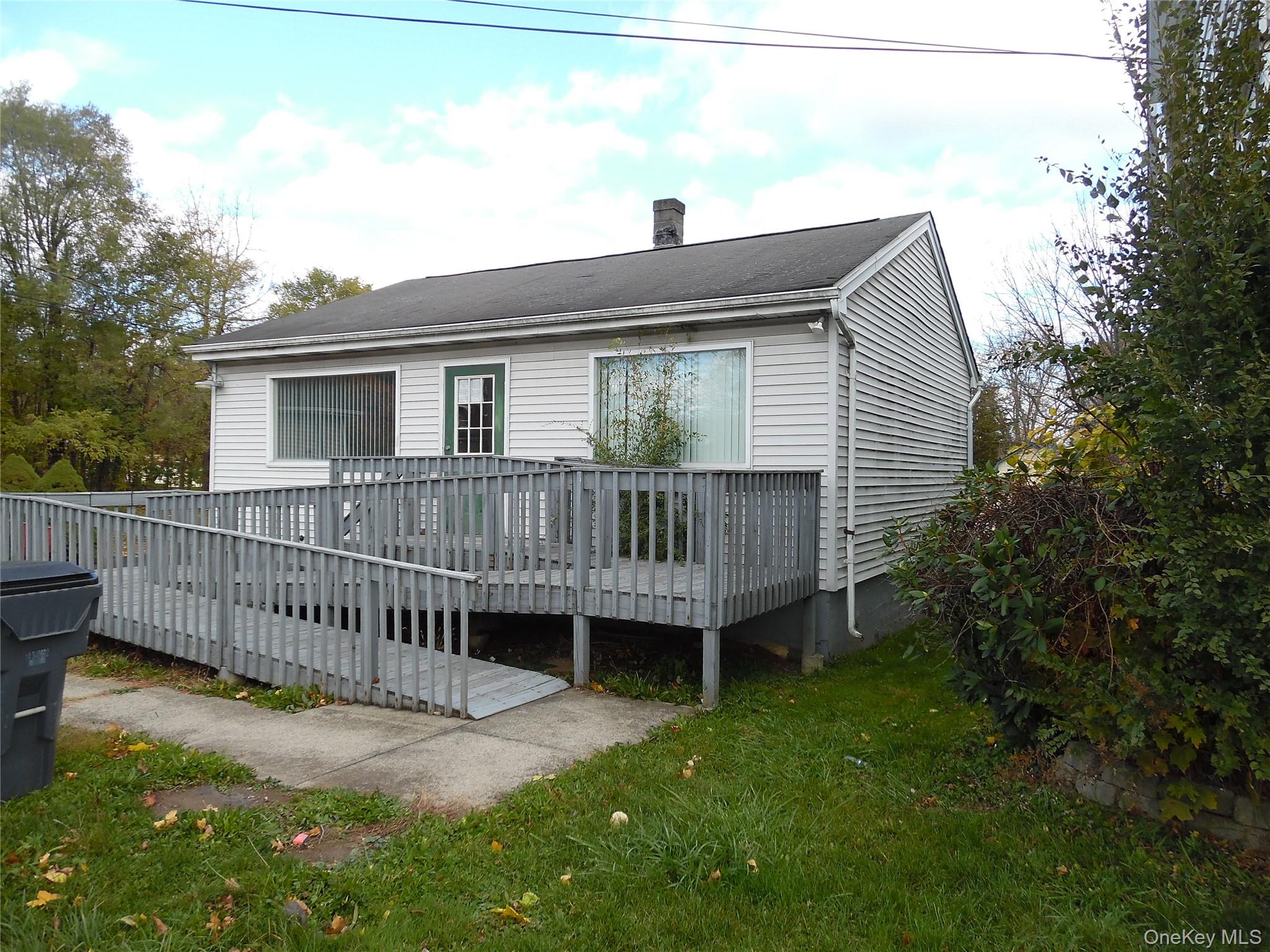 Back of house with a deck, a chimney, and a lawn