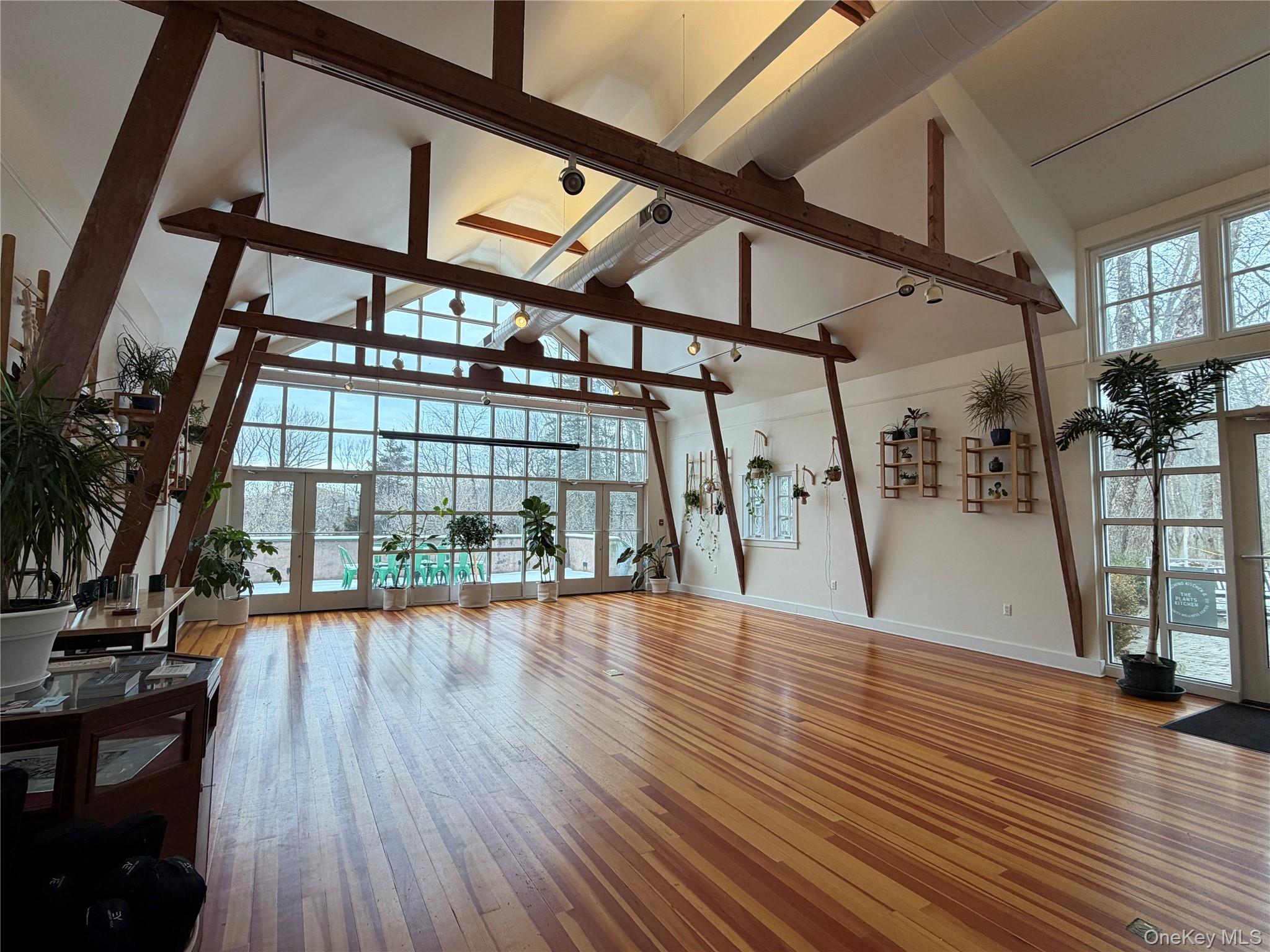 Unfurnished living room with high vaulted ceiling, light wood-style flooring, plenty of natural light, a skylight, and french doors