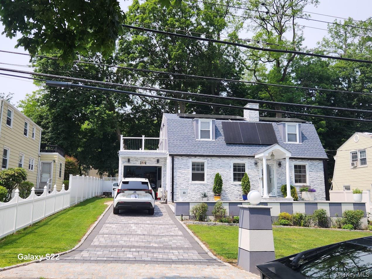 View of front of property featuring stone siding, roof with shingles, a chimney, an attached garage, and roof mounted solar panels