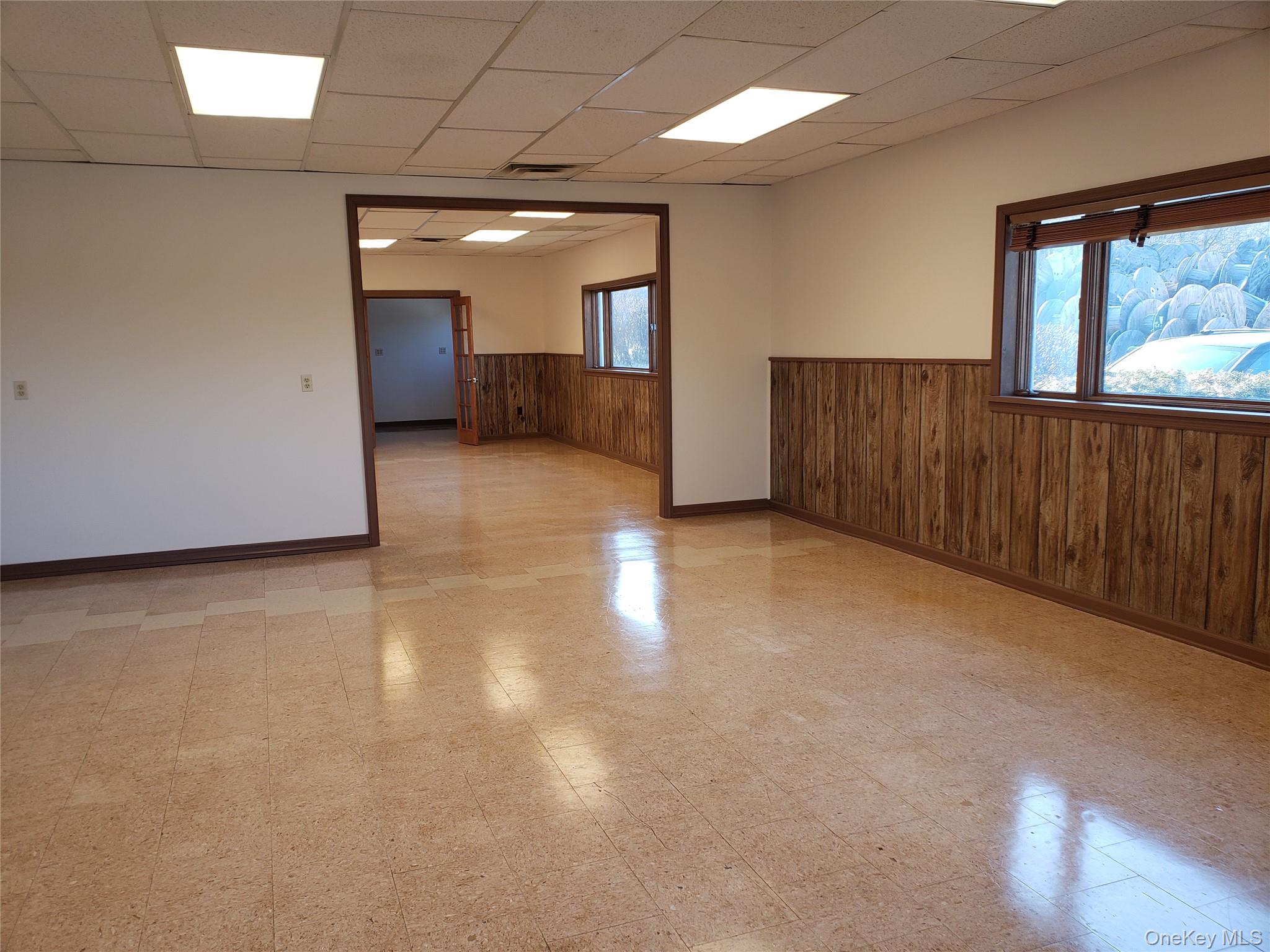 Empty room with light flooring, wood walls, a drop ceiling, and wainscoting