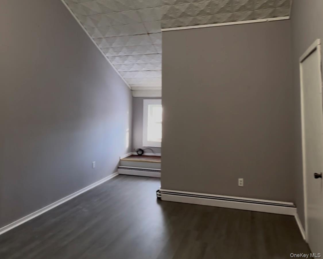 Spare room featuring baseboard heating and dark wood-style floors