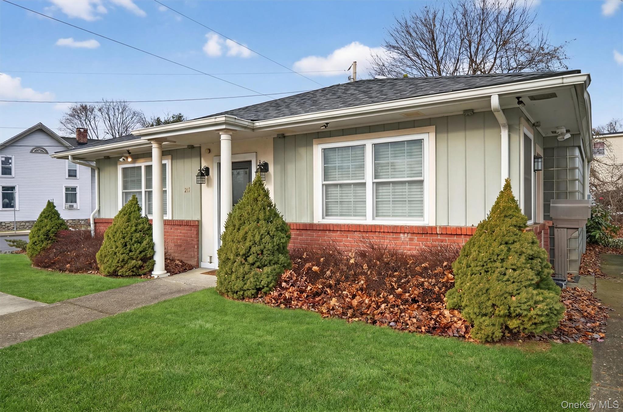 View of front of property featuring brick siding, board and batten siding, a front yard, a shingled roof, and covered porch