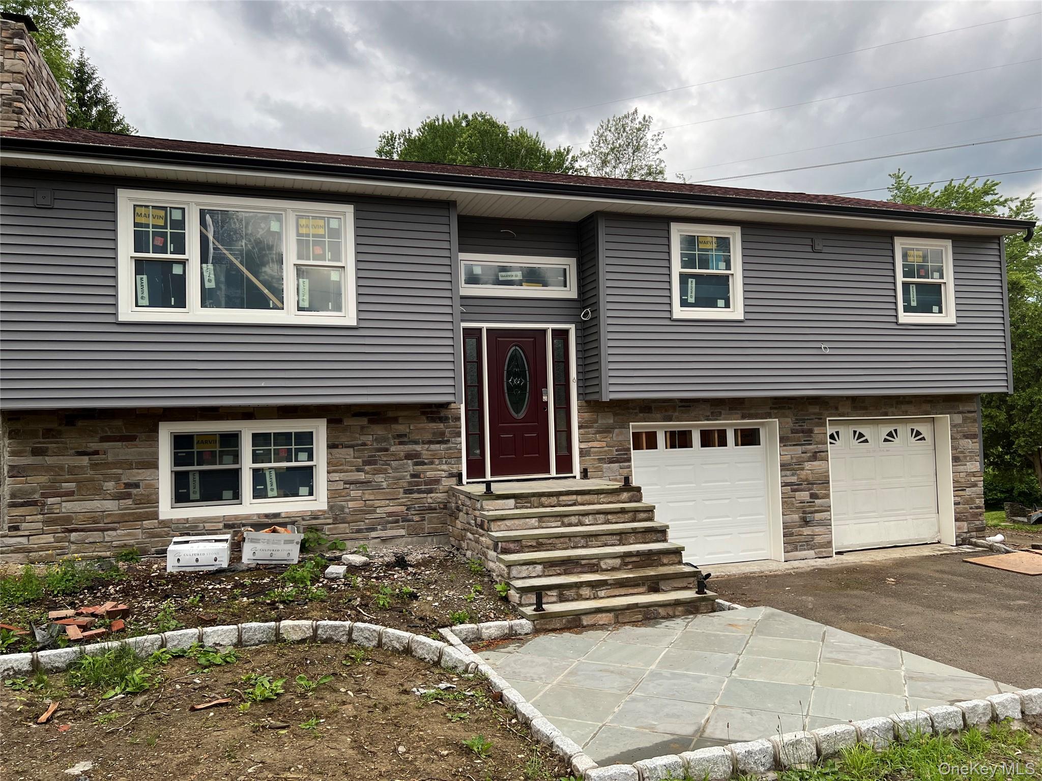 Raised ranch with driveway, a garage, stone siding, entry steps, and a chimney