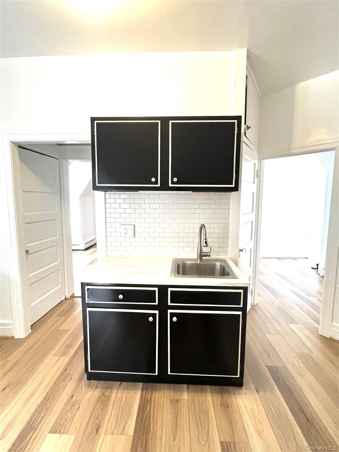Kitchen featuring dark cabinetry, light countertops, light wood finished floors, and decorative backsplash