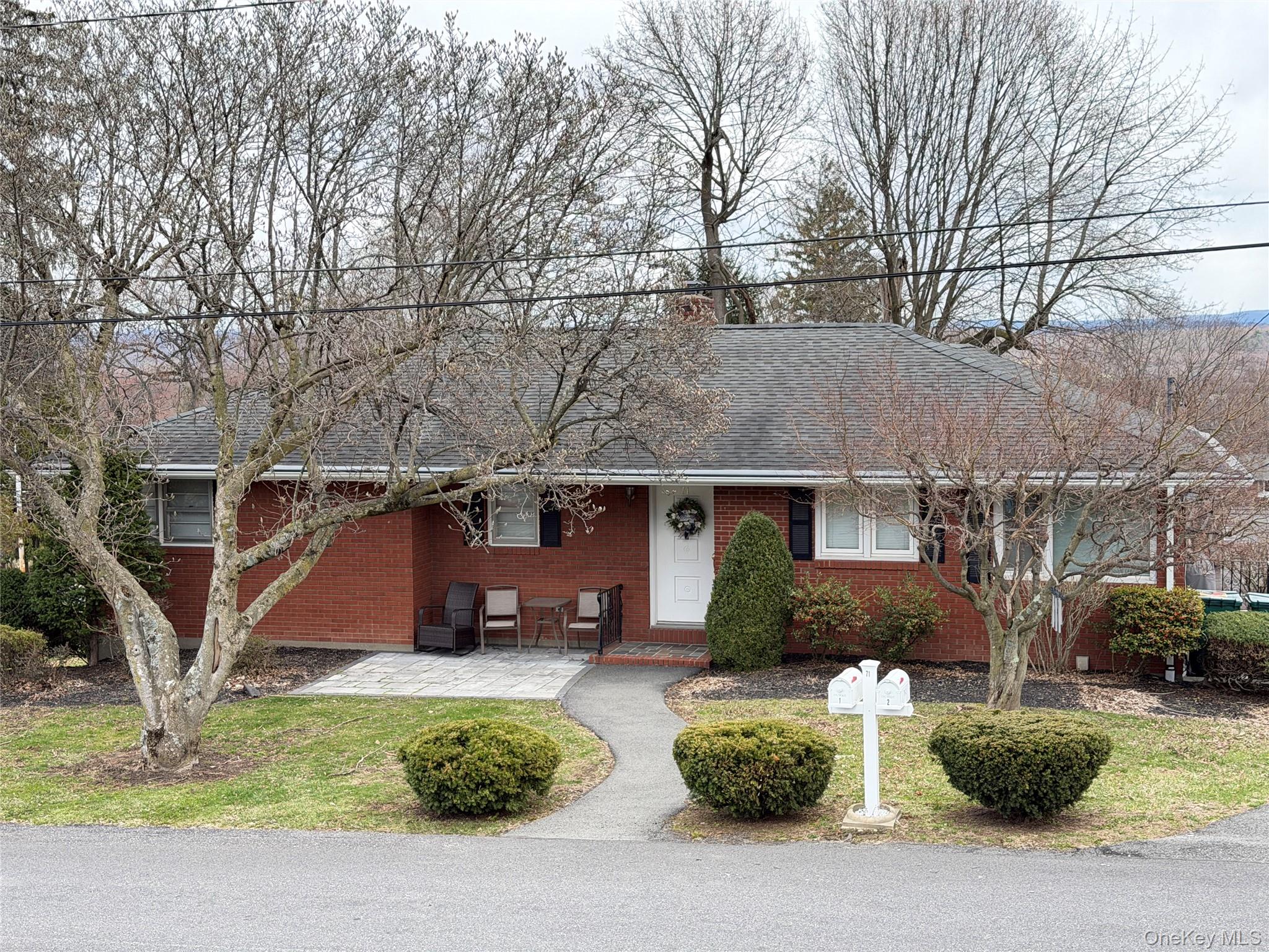 Ranch-style house with brick siding, a shingled roof, a front lawn, a chimney, and a patio area