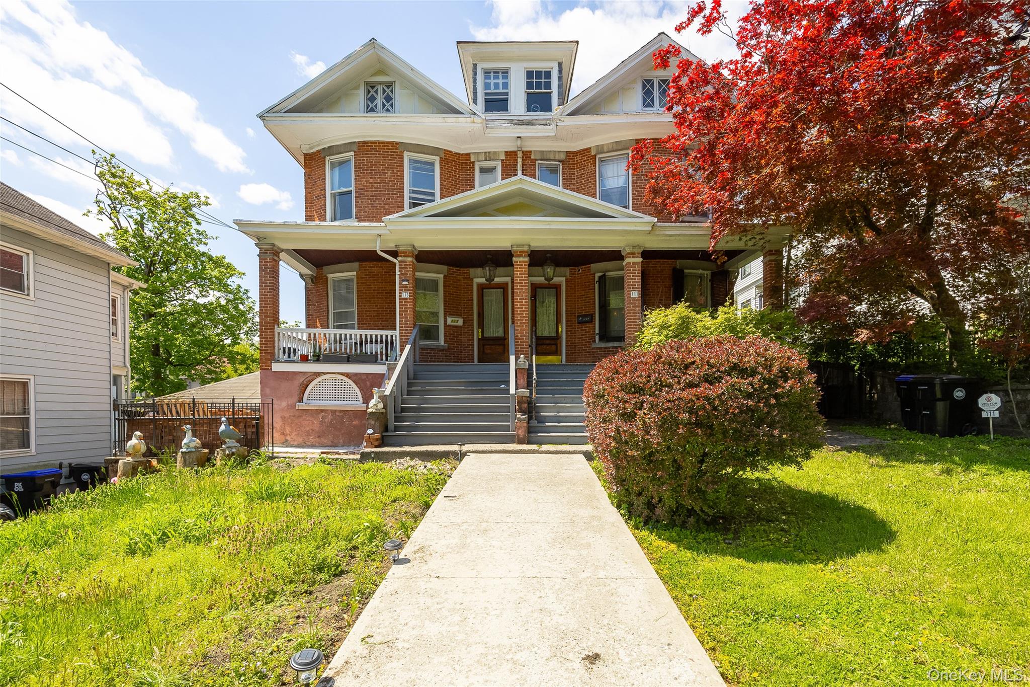 Brick multi-story residence featuring a covered front porch with multiple entry points, white railings, and column supports