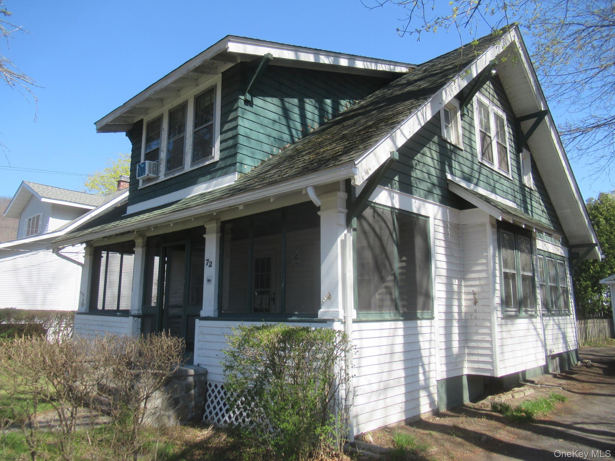 Craftsman-style home featuring a covered front porch, white shingle siding, green shake siding, a multi-gabled roofline, and visible window framing