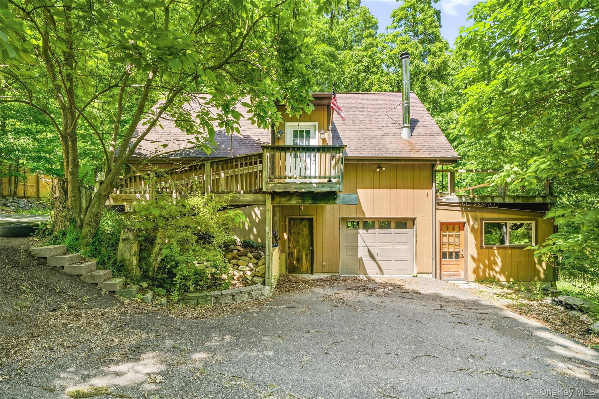Rustic exterior featuring a deck, two garage bays, and a secondary balcony