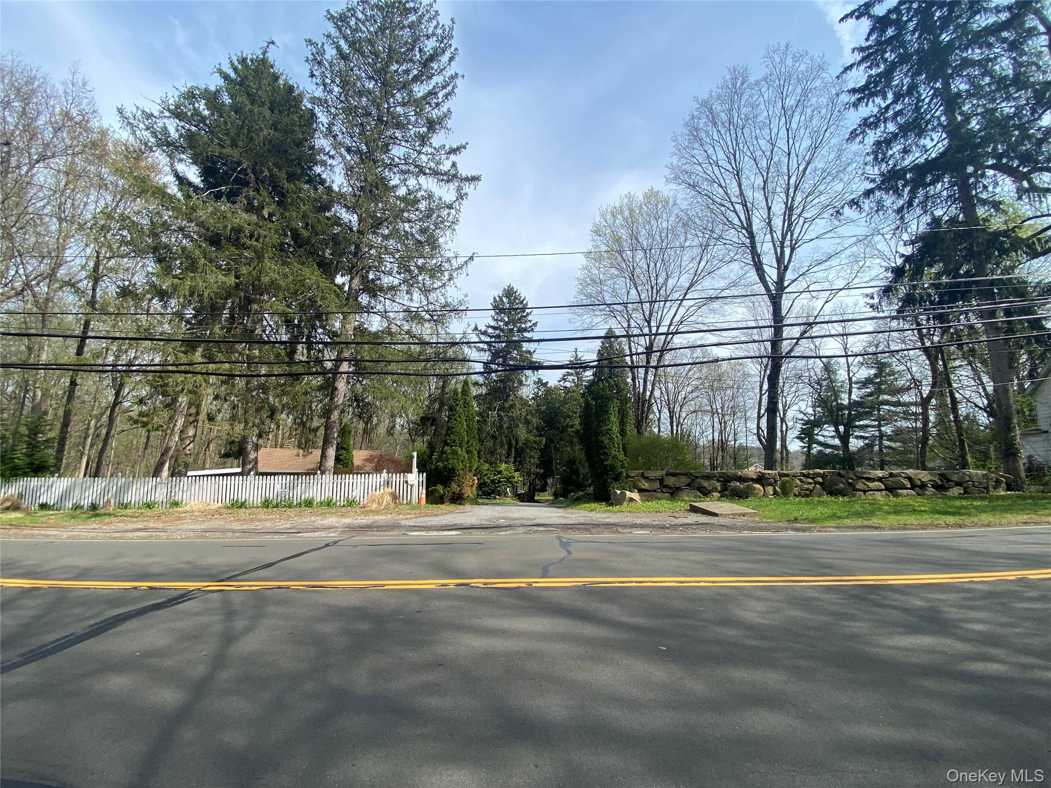 Private lot featuring mature trees, a natural stone retaining wall, and a white picket fence
