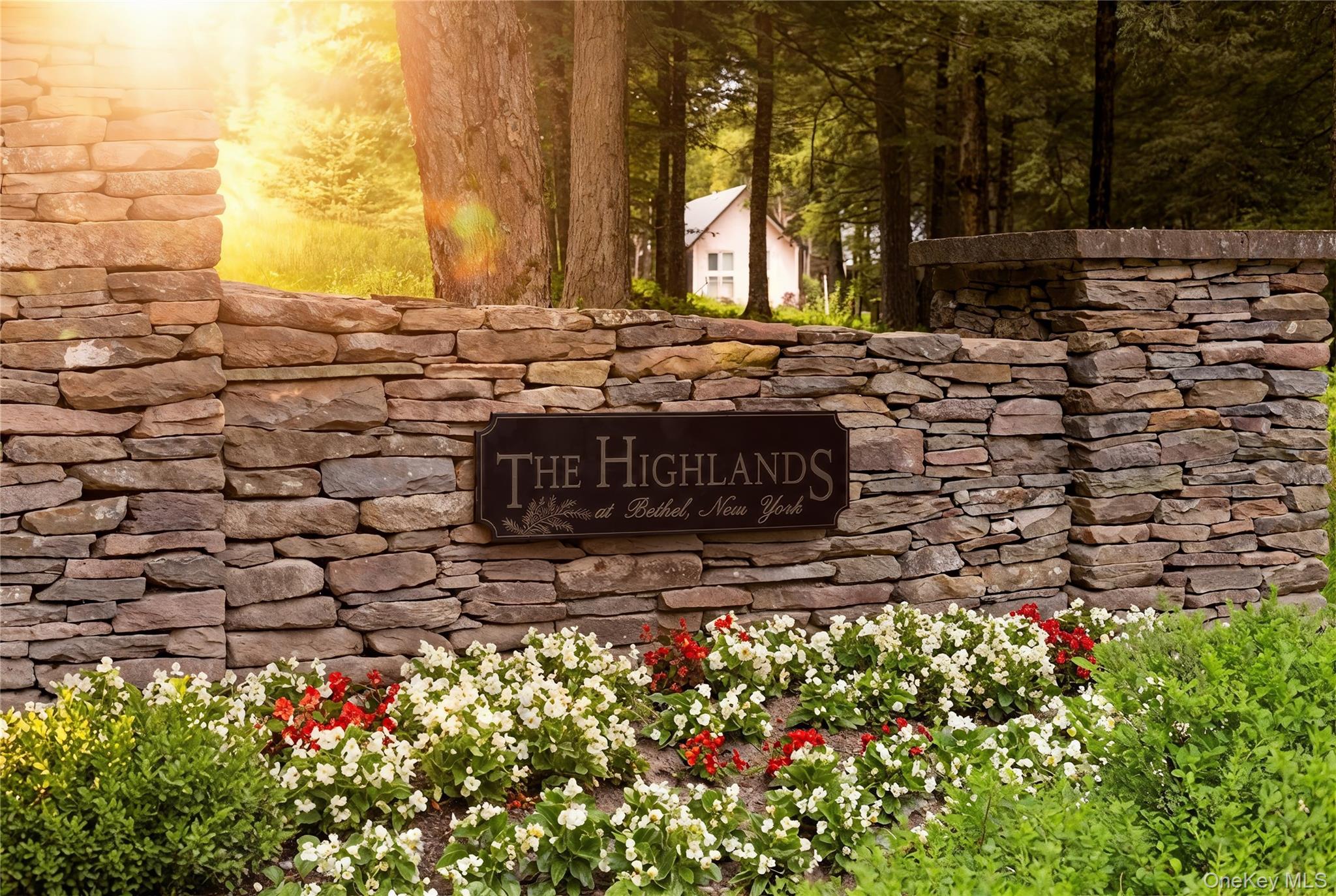 Stone entrance wall with a dark metal plaque, featuring manicured flower beds and established greenery
