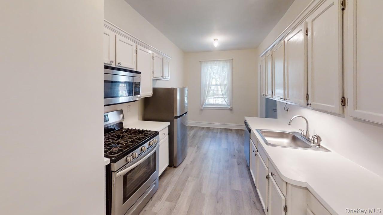 Kitchen featuring stainless steel appliances, wood-finish flooring, white cabinetry, white countertops, and a stainless steel sink