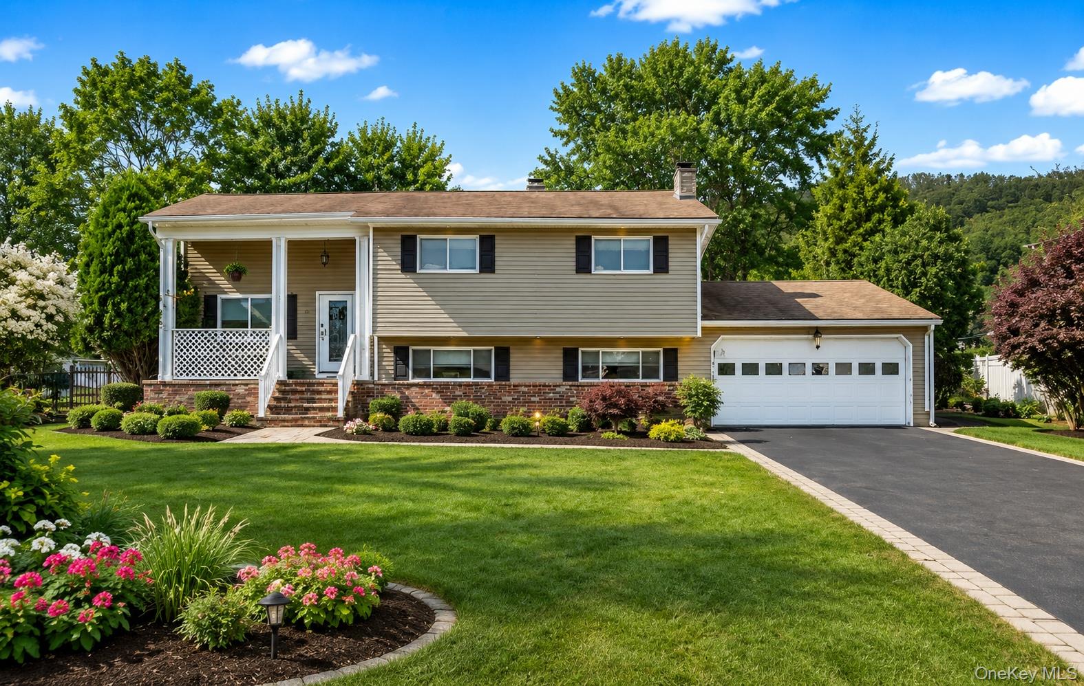 Split-level residence featuring a covered front porch with white railings, a two-car garage, and a paved driveway with stone paver edging