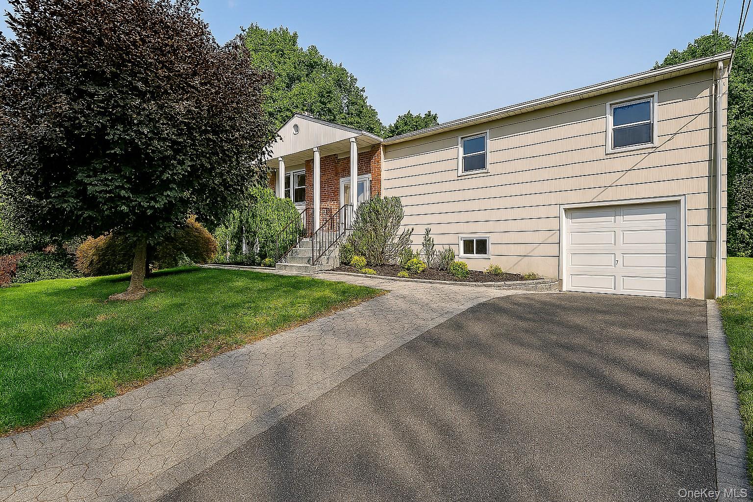 Raised Ranch featuring a brick facade with columned portico, an attached single-car garage, and a paved driveway
