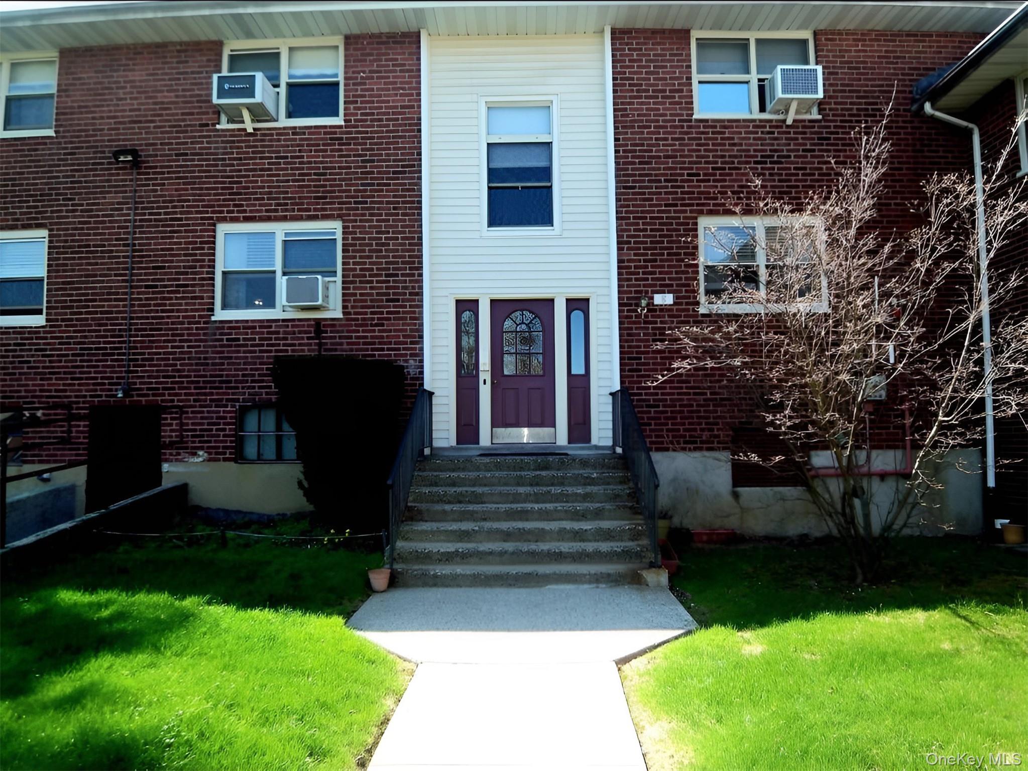 Brick facade building with a prominent central entrance featuring a decorative glass door, flanked by white siding