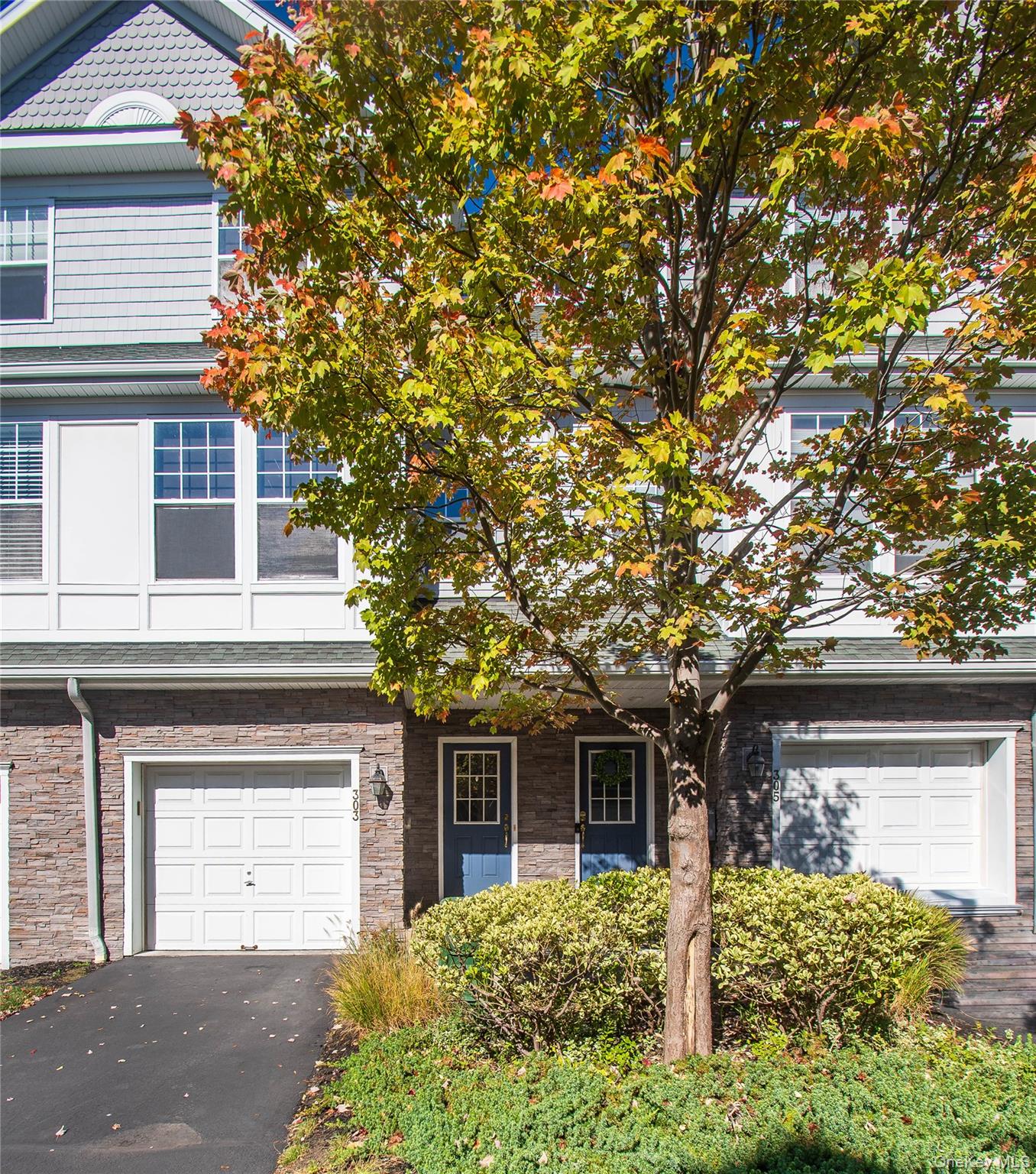 View of front of home with stone siding, asphalt driveway, a garage, and a porch