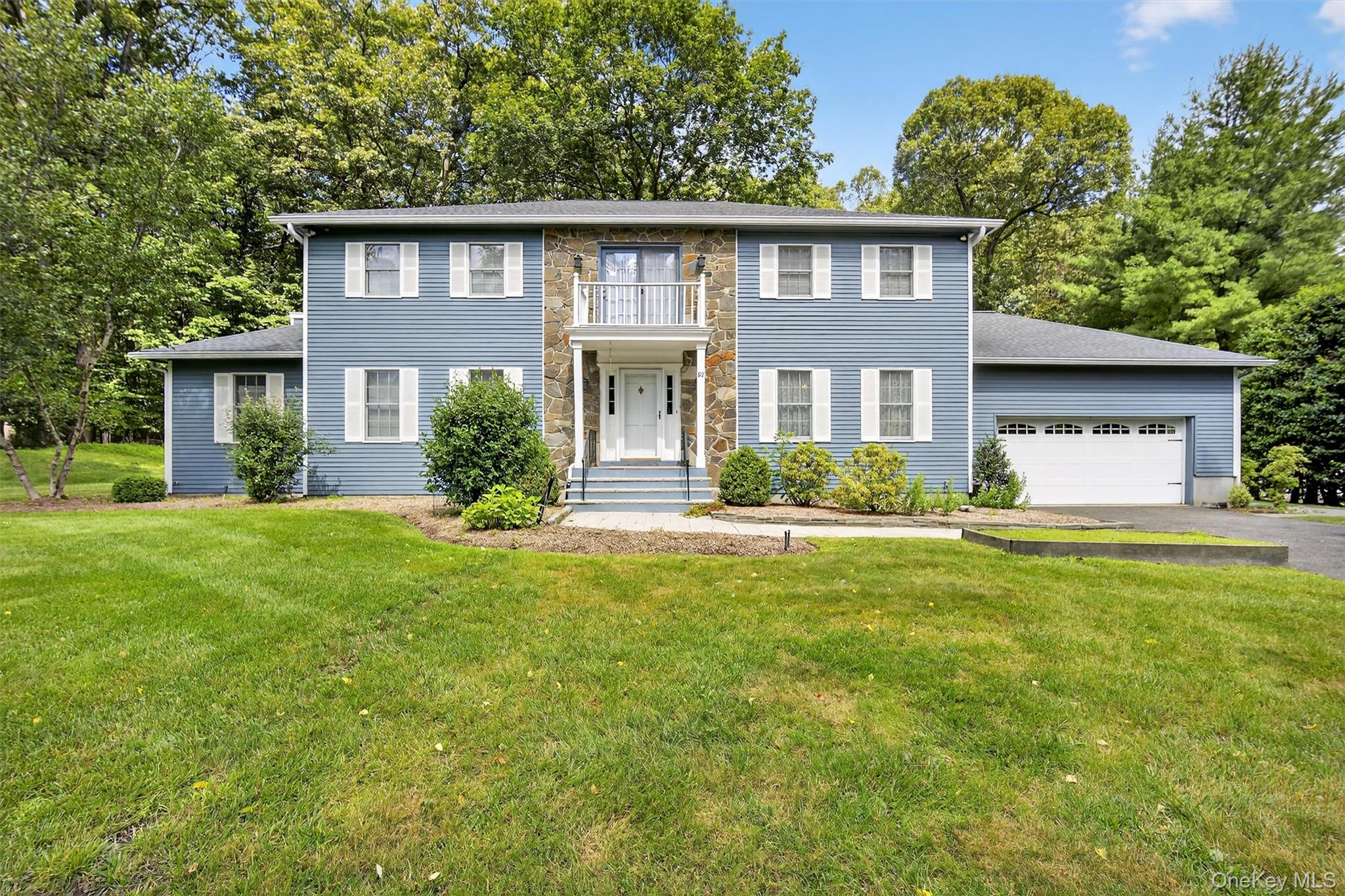 View of front facade with asphalt driveway, a balcony, an attached garage, and a front lawn