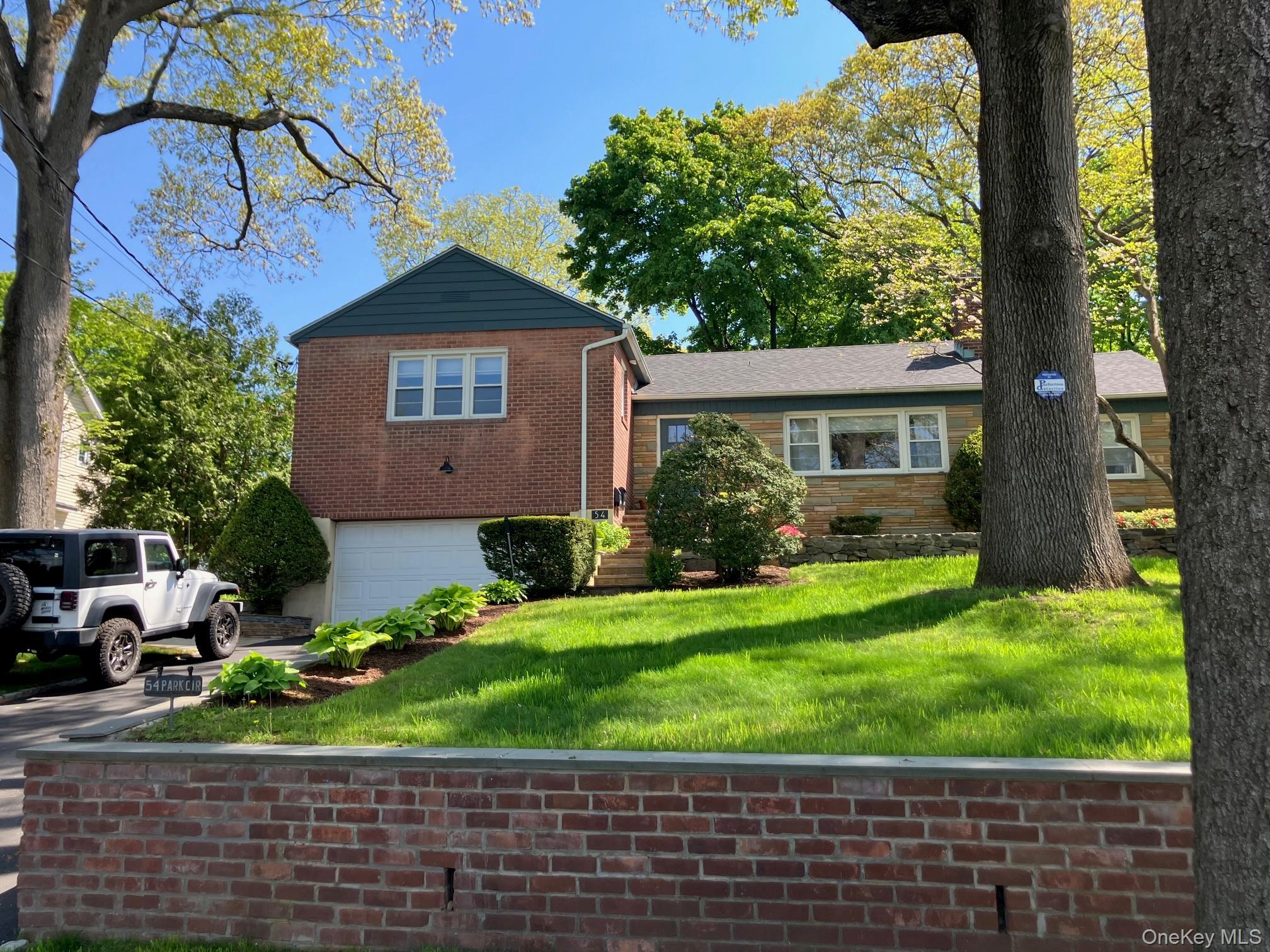 Split-level residence featuring a brick and stone facade, attached garage, and a sloped, manicured lawn