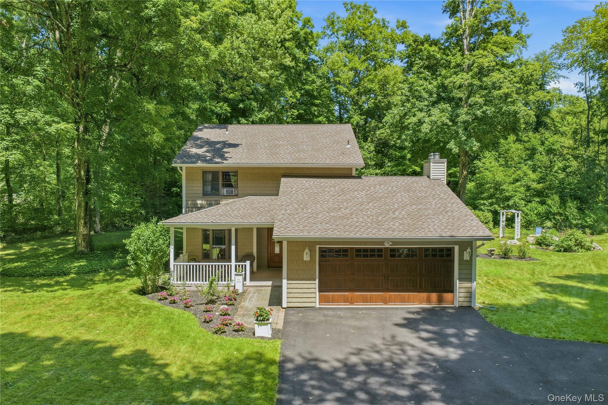 Two-story residence featuring siding exterior, an attached garage with a wood-finish door, and a covered front porch with white railings