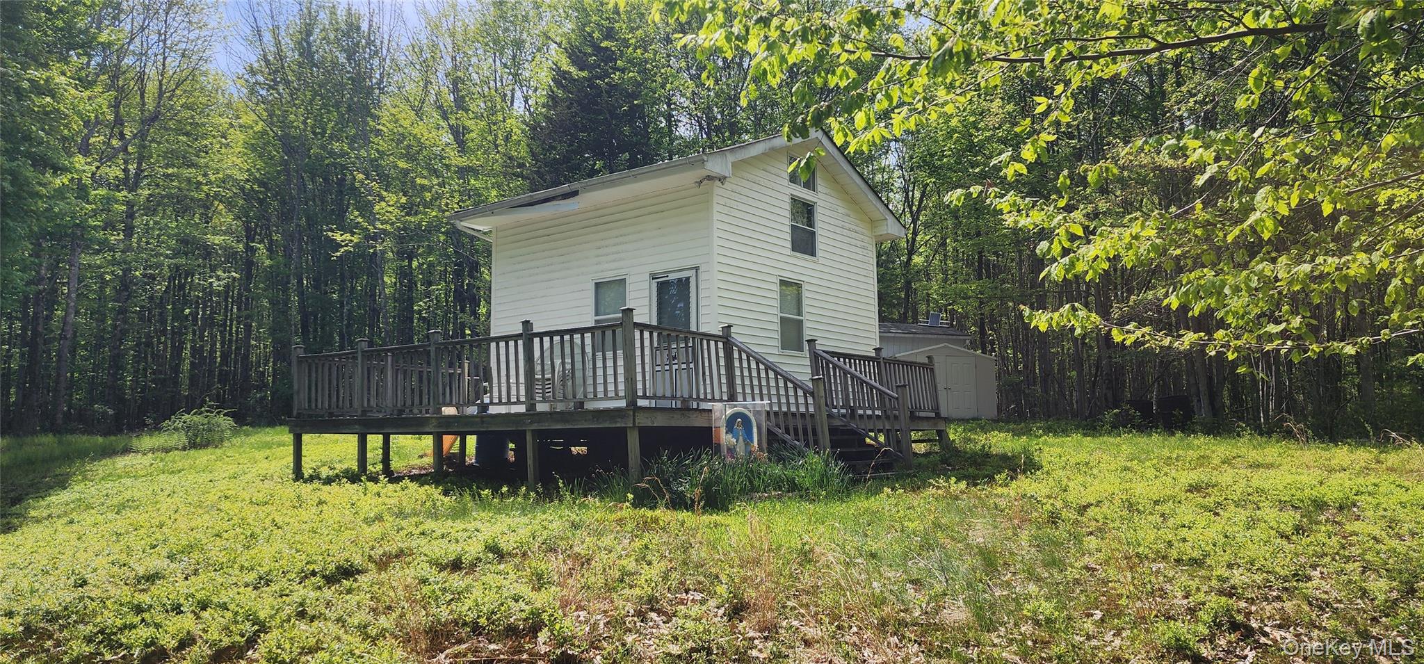 View of home's exterior with a storage unit, a wooden deck, an outdoor structure, and a view of trees